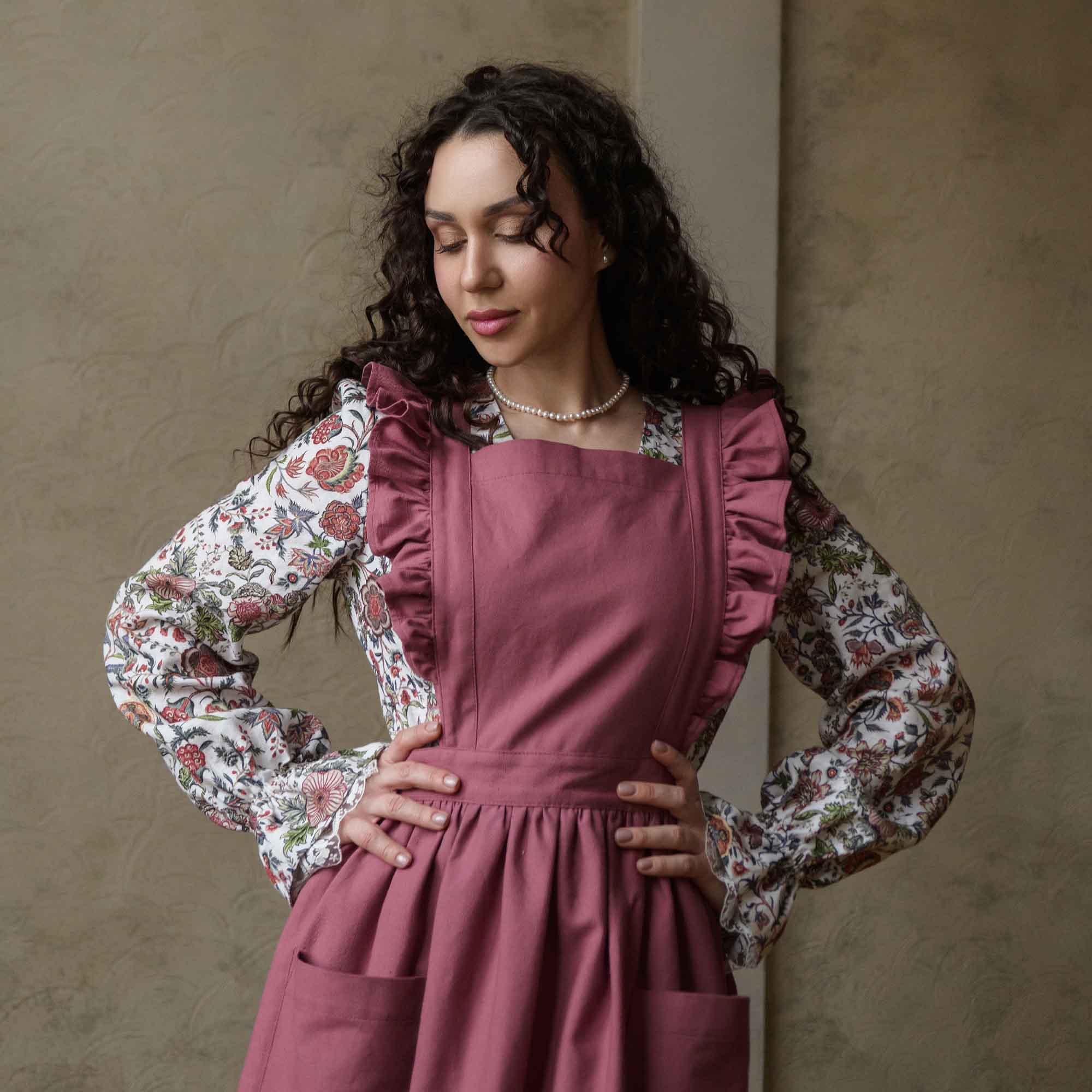 Woman wearing a pink apron with floral sleeves against a beige wall