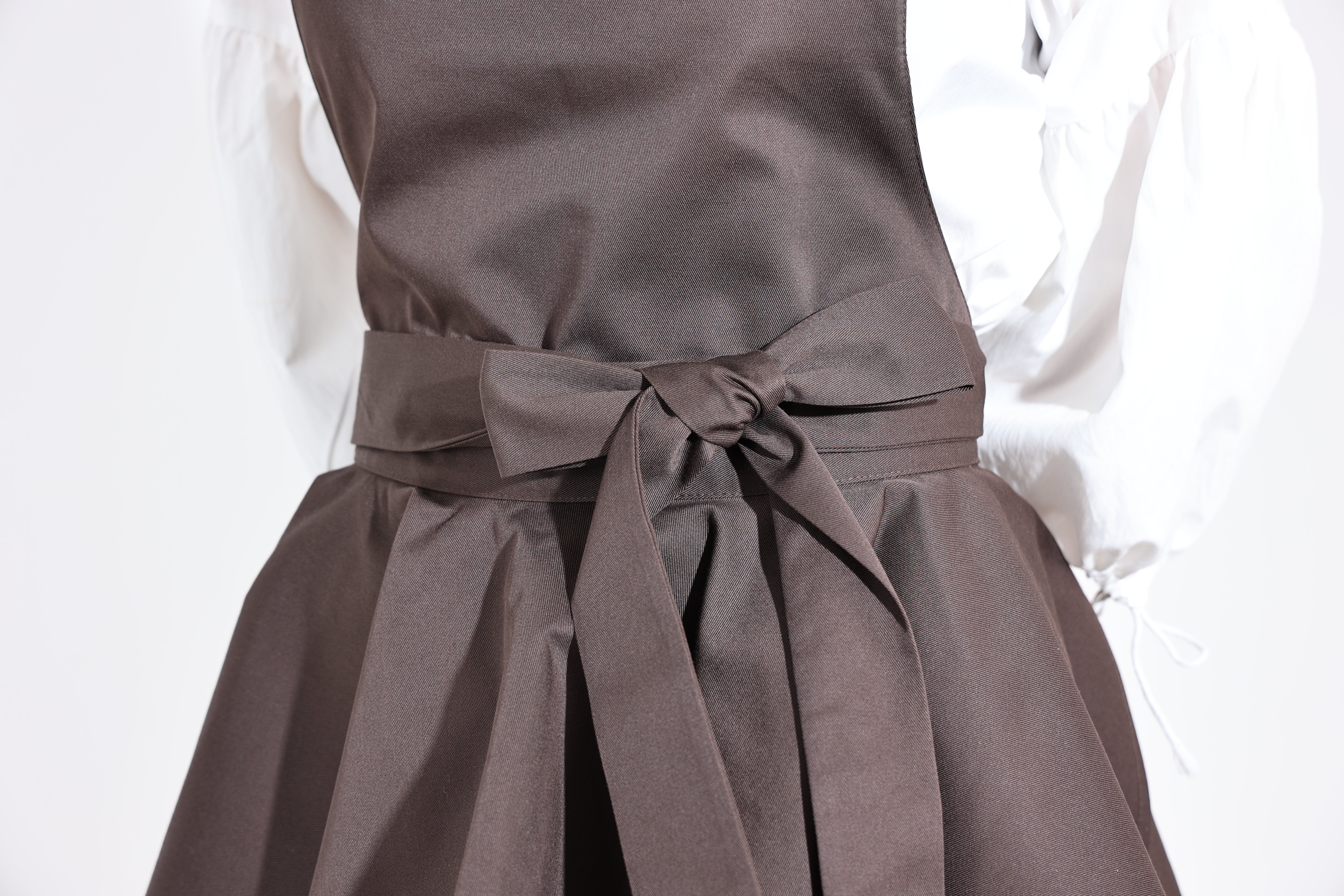 Close-up of the waist bow and pleated ruffle on the dark brown apron