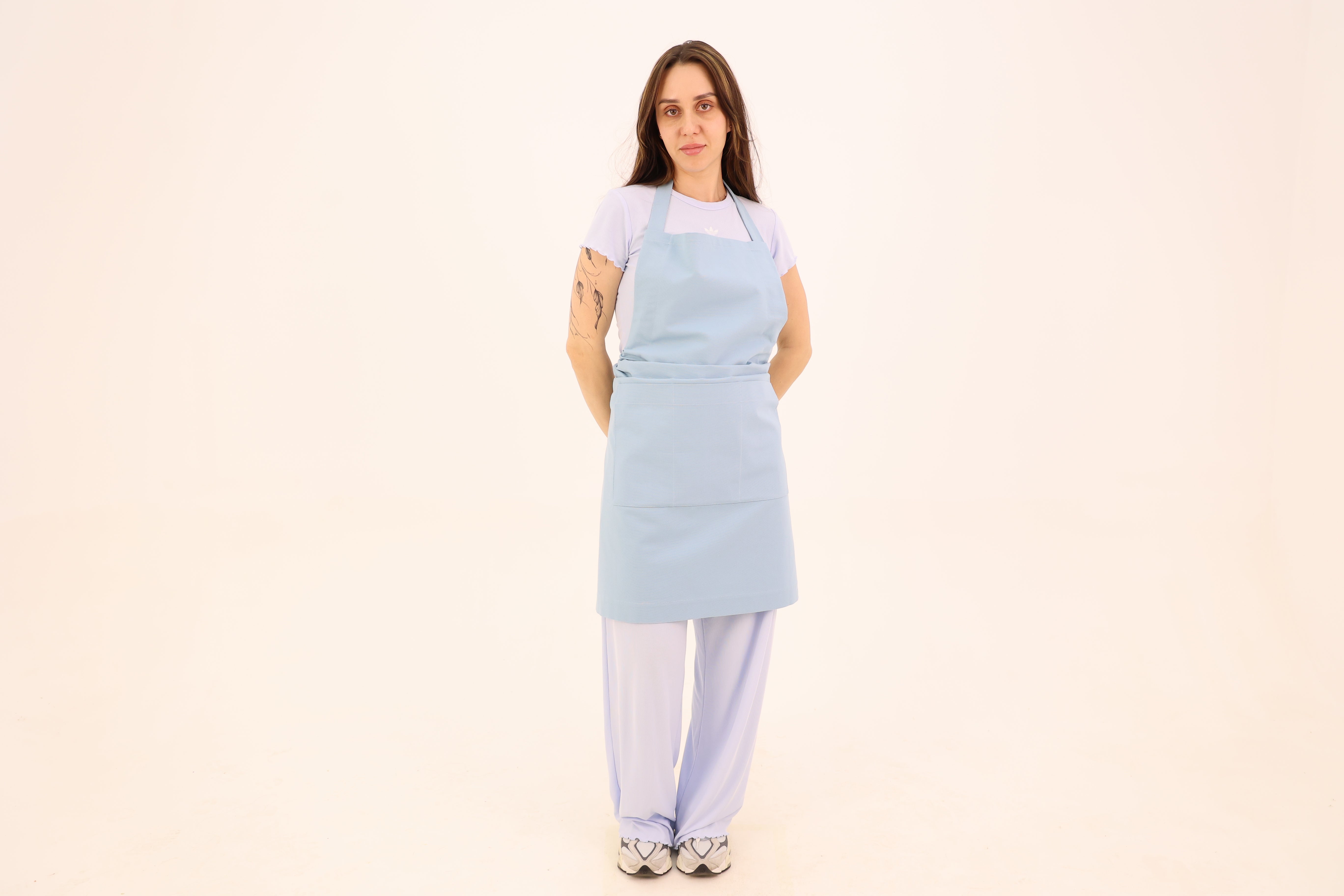 Woman wearing a powder blue cotton bib apron with a wide waist sash