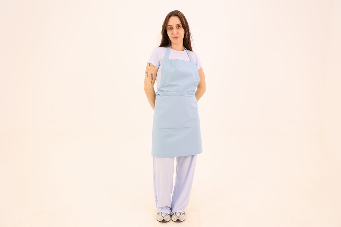 Woman wearing a powder blue cotton bib apron with a wide waist sash