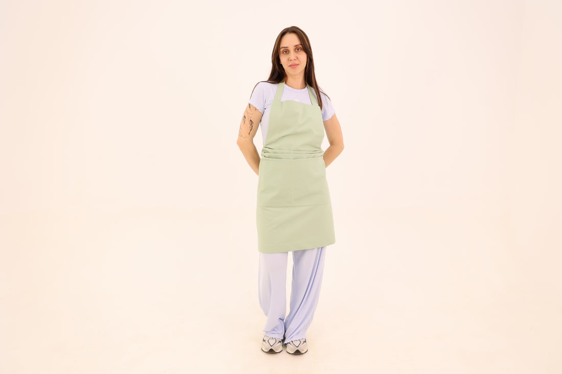 Woman wearing a sage green cotton bib apron with a wide waist sash