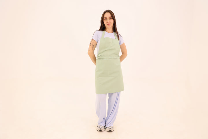 Woman wearing a sage green cotton bib apron with a wide waist sash