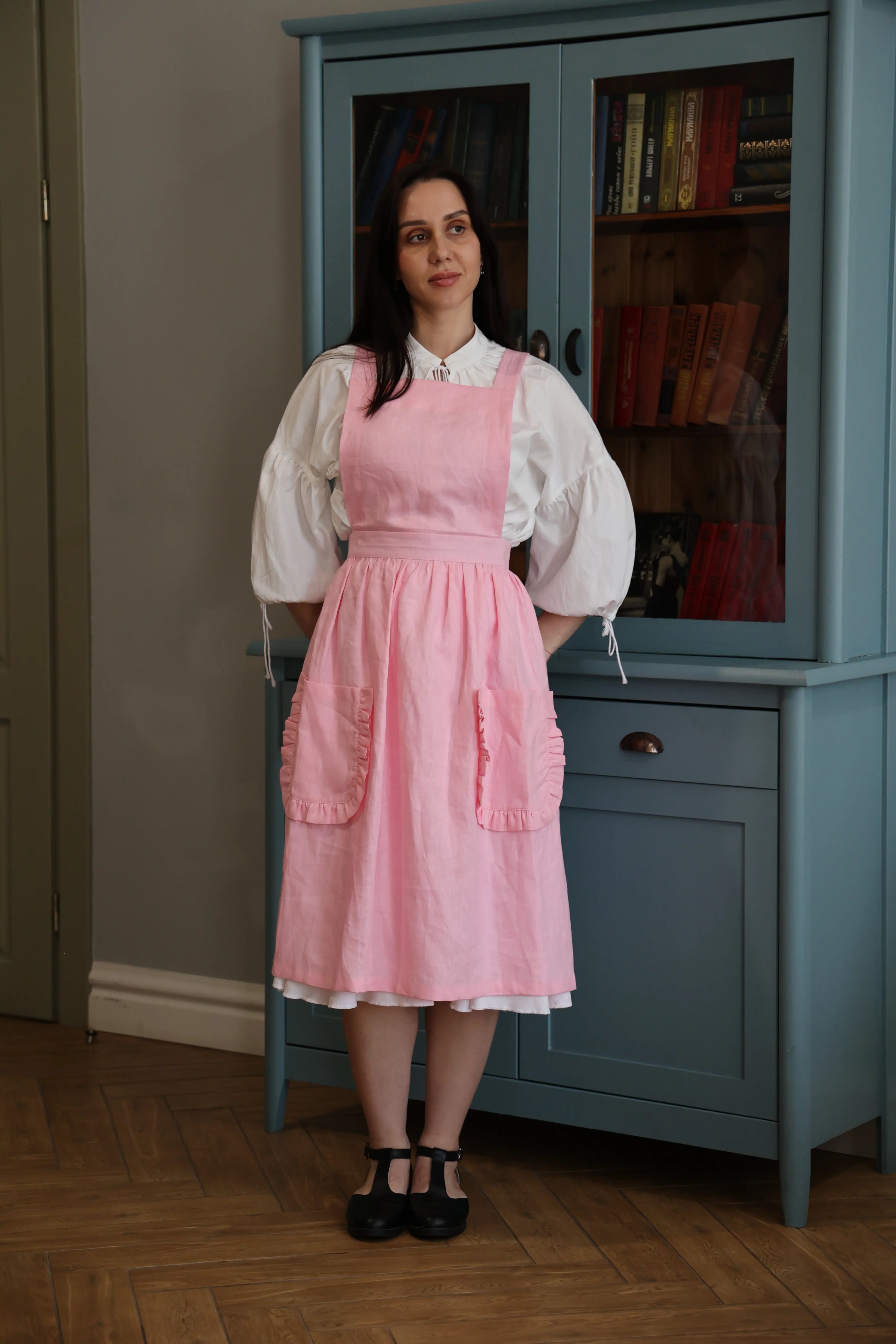 Woman wearing a soft pink crossback apron with ruffled pockets