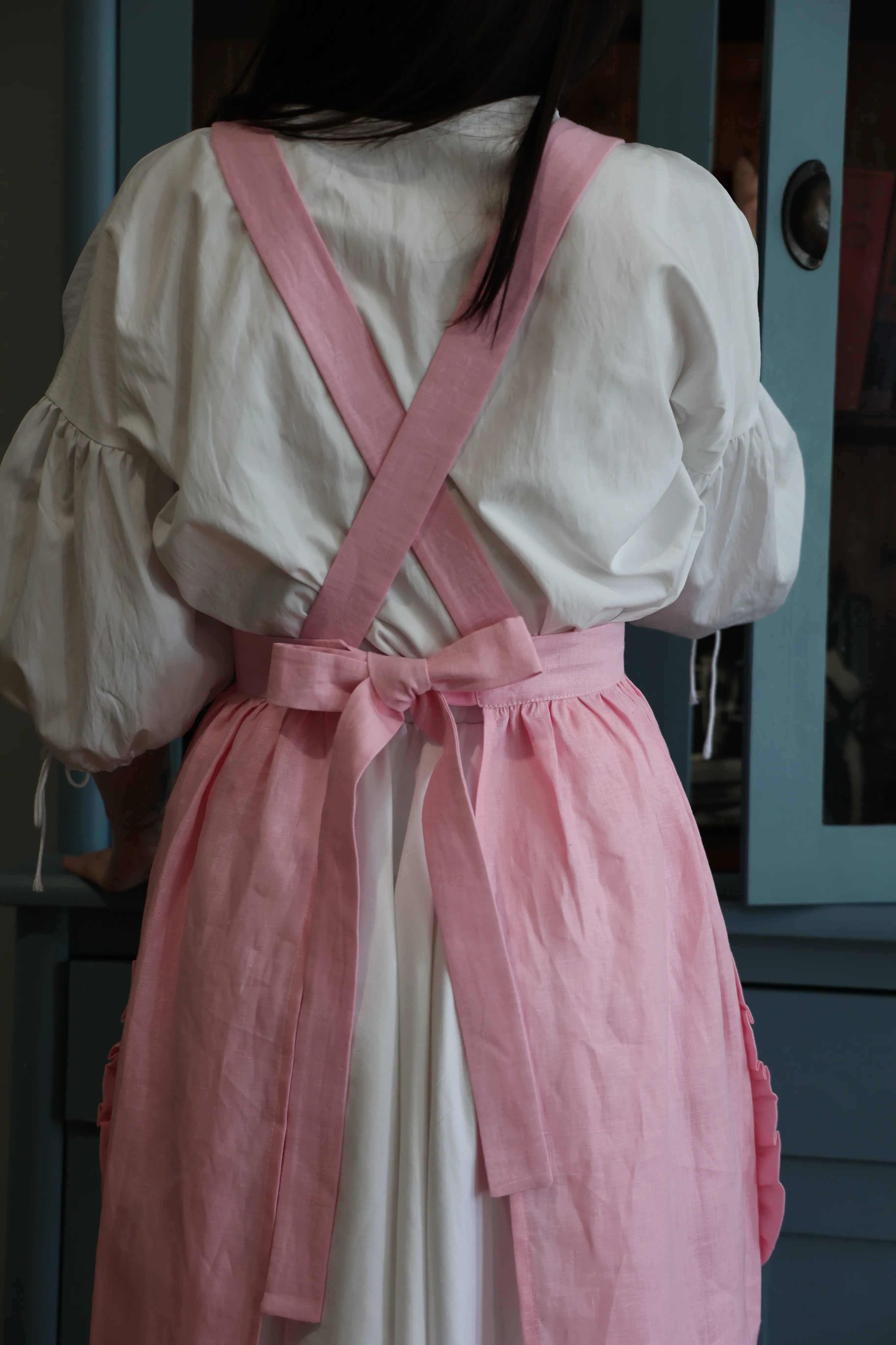 Back view of the soft pink apron with crossback straps and a bow