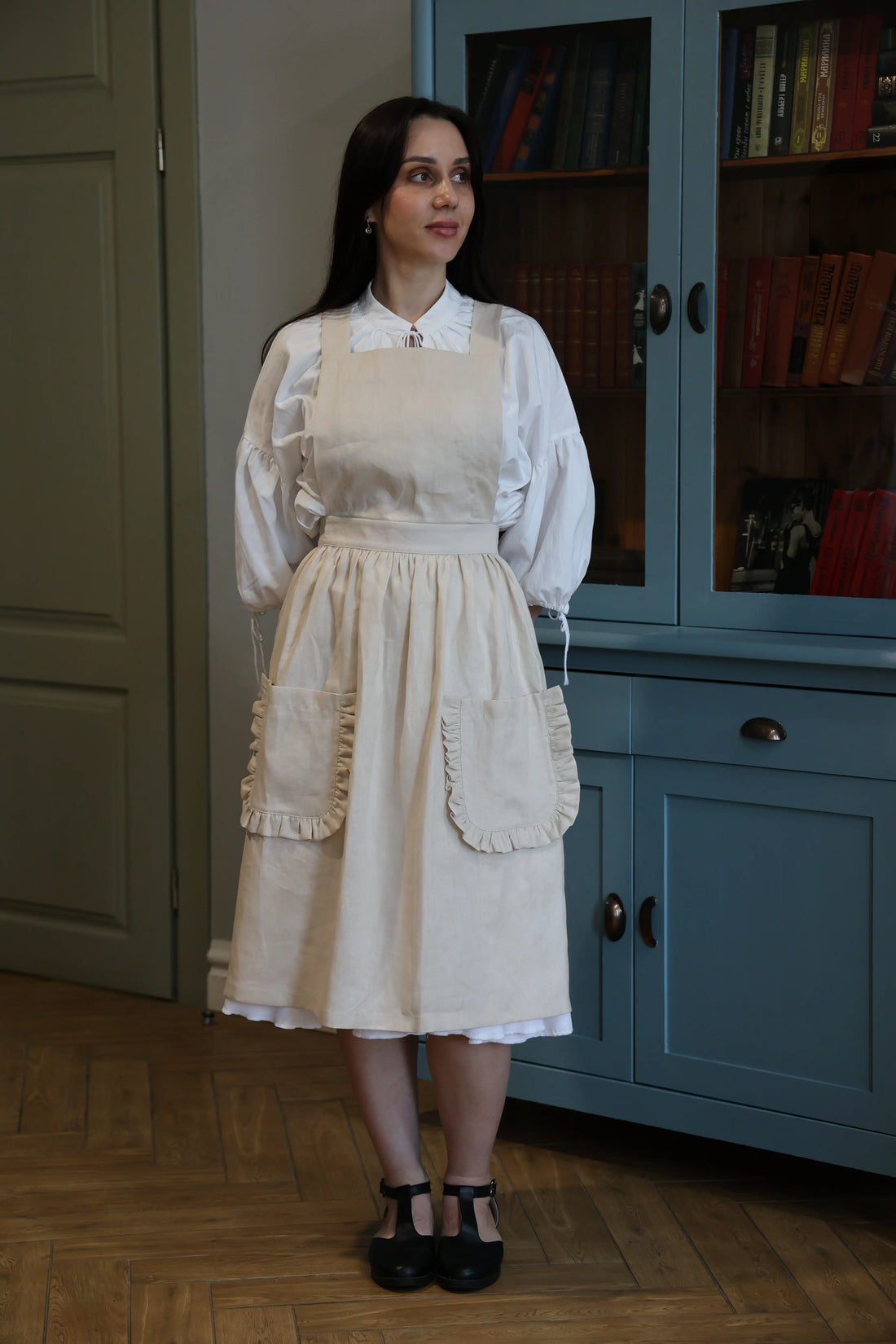 Woman in the sand ruffle apron in front of a blue kitchen cabinet
