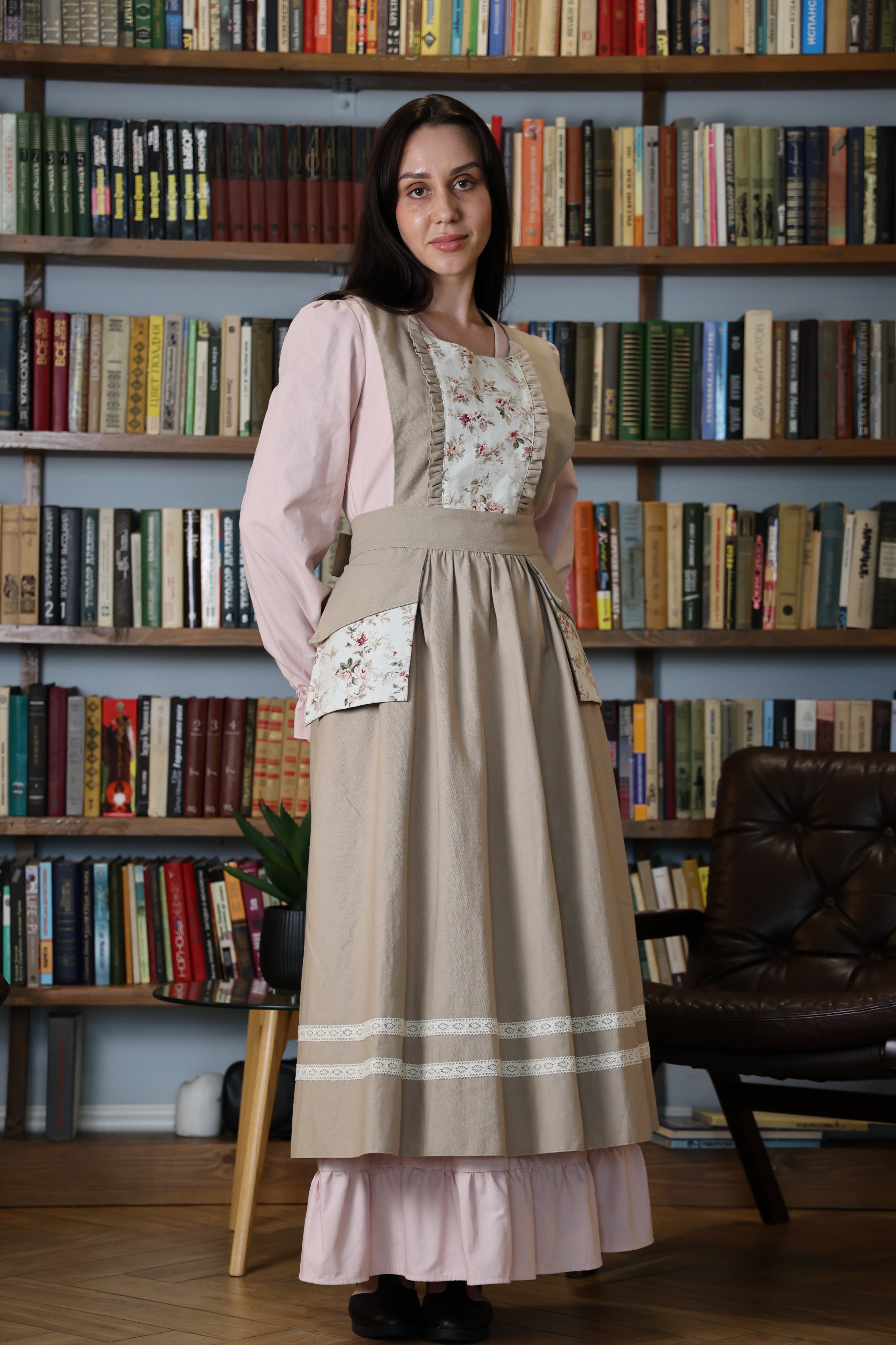 Woman wearing the beige floral pinafore apron in front of bookshelves