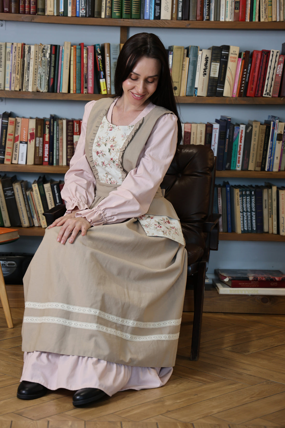 Woman in the beige floral pinafore apron seated in an armchair