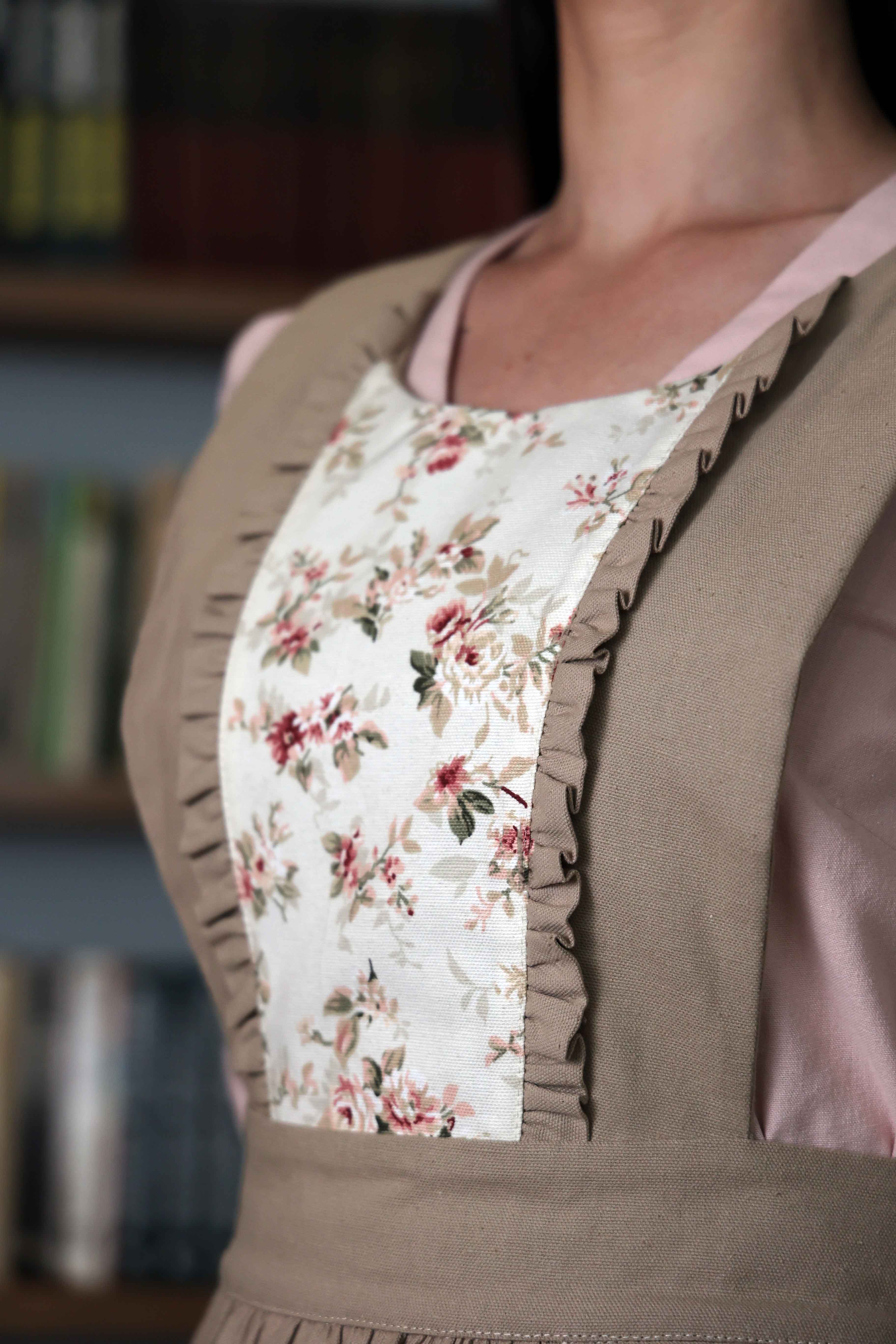 Close-up of the floral bib panel with ruffle trim on the beige apron