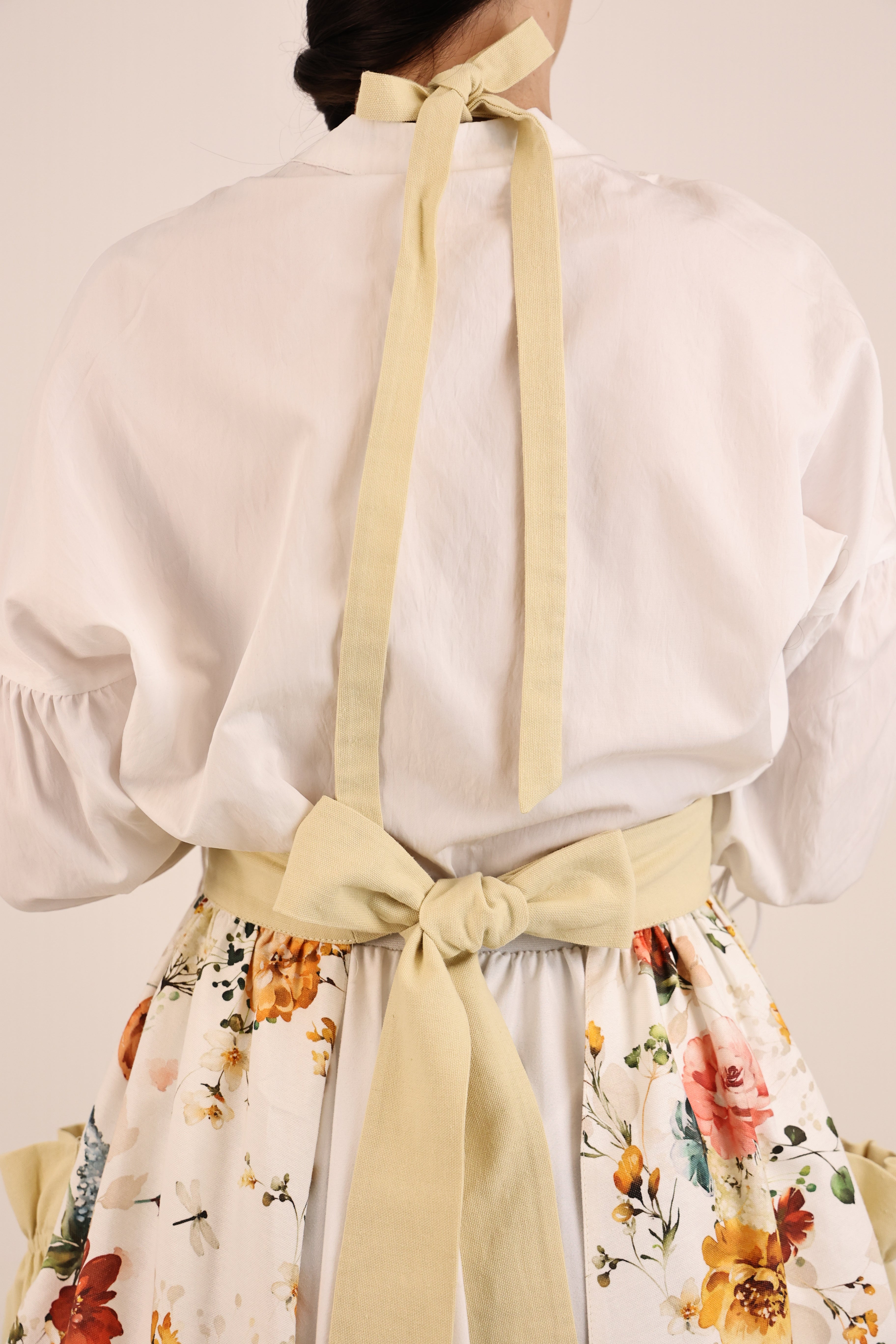 Person wearing a white blouse with floral skirt and yellow ribbon, on a plain background