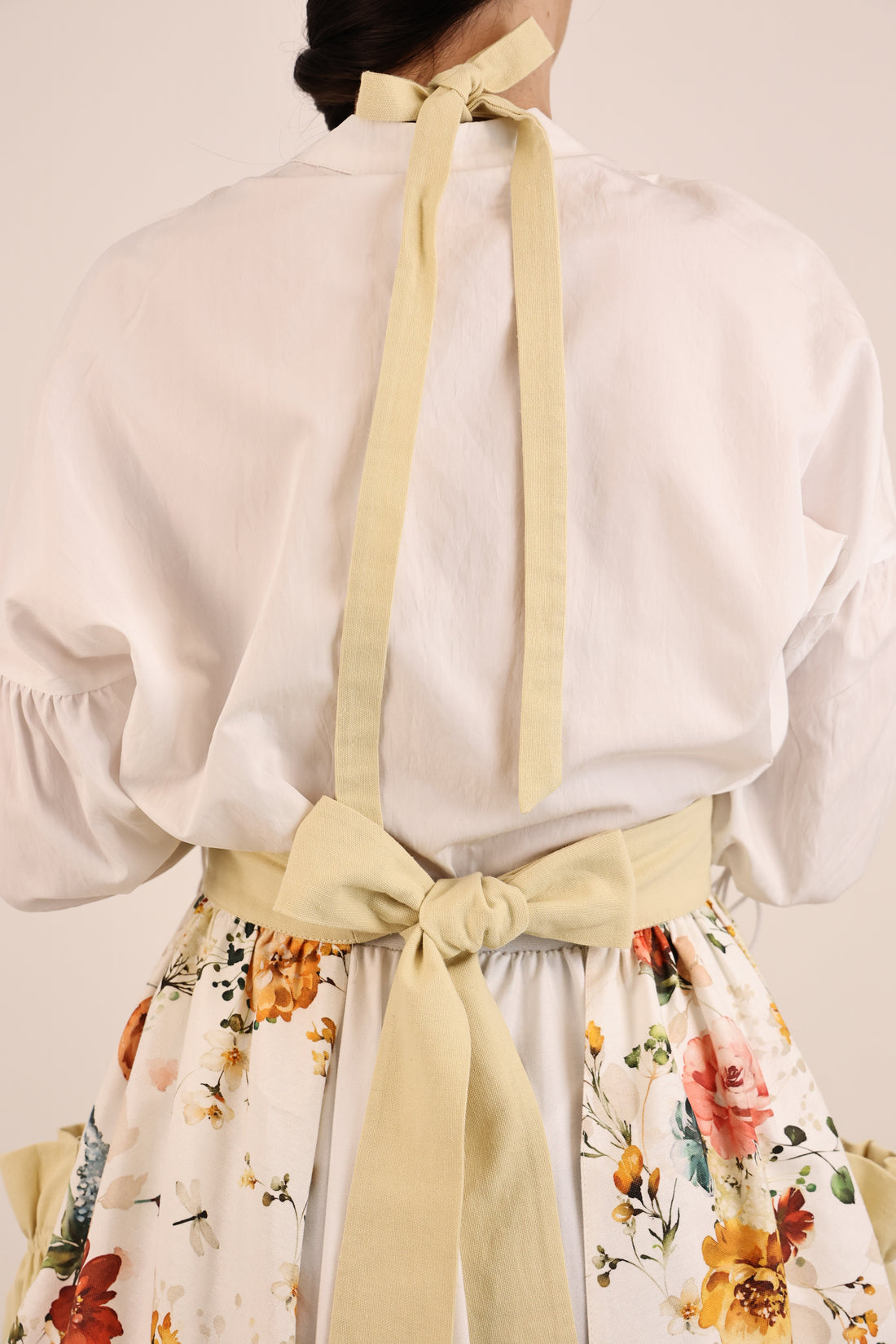 Person wearing a white blouse with floral skirt and yellow ribbon, on a plain background