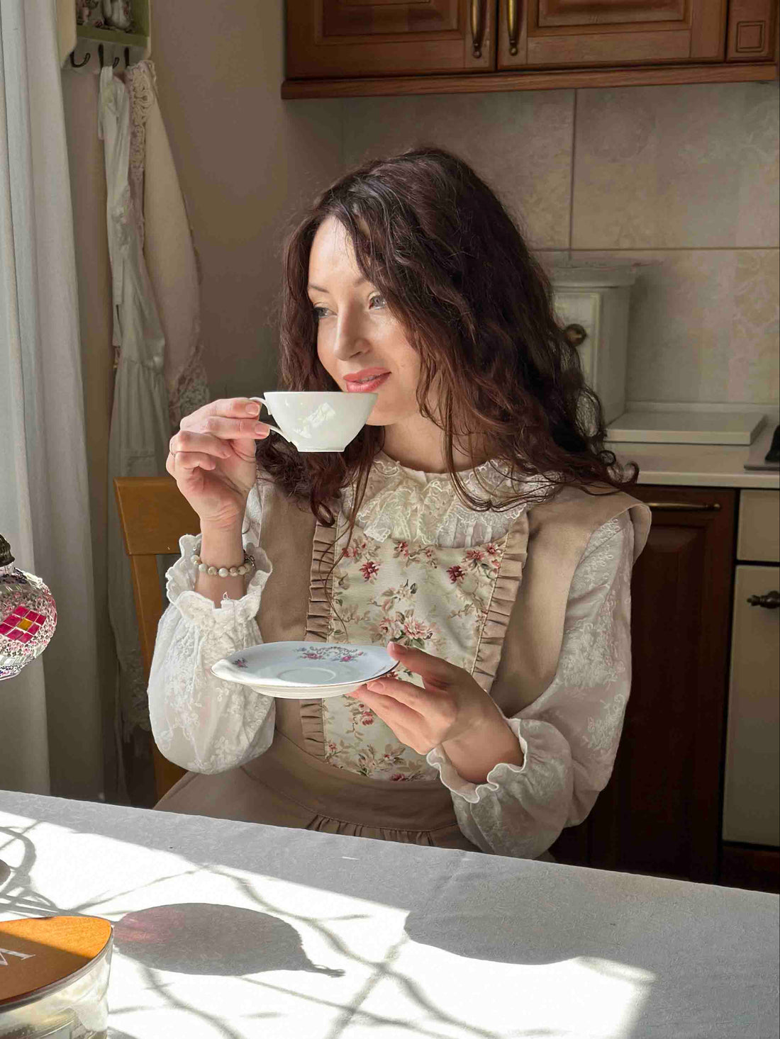 Woman sitting at a kitchen table drinking from a teacup