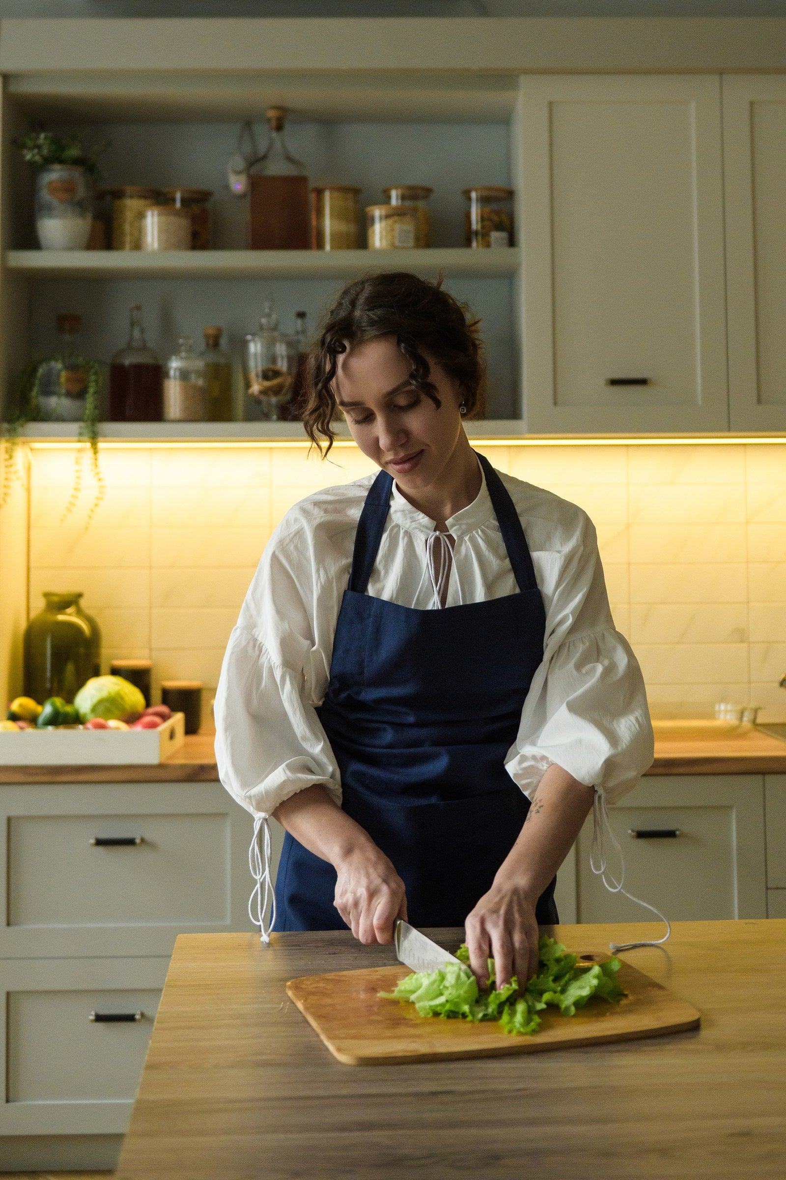 Woman in a navy blue cotton bib apron chopping salad at a kitchen island