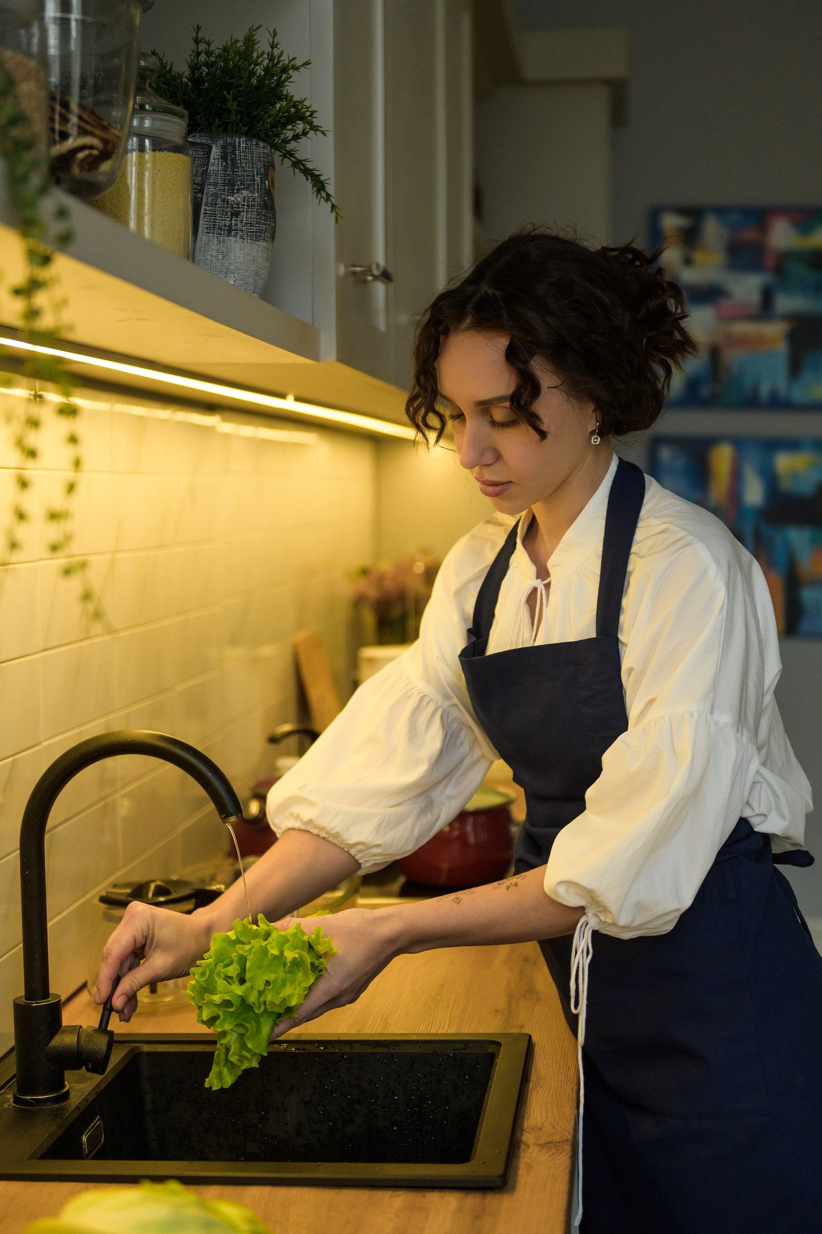 Side view of the navy blue bib apron while washing lettuce at the sink
