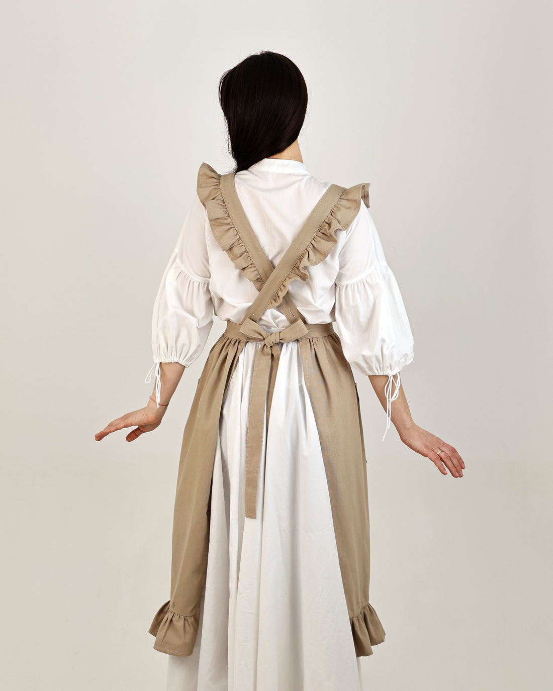 Person wearing a white blouse and beige overalls on a plain background