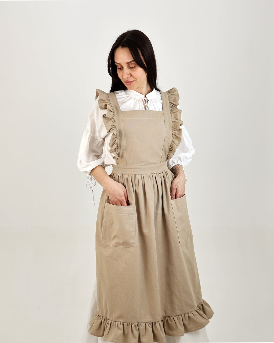 Woman wearing a beige apron over a white blouse on a plain background