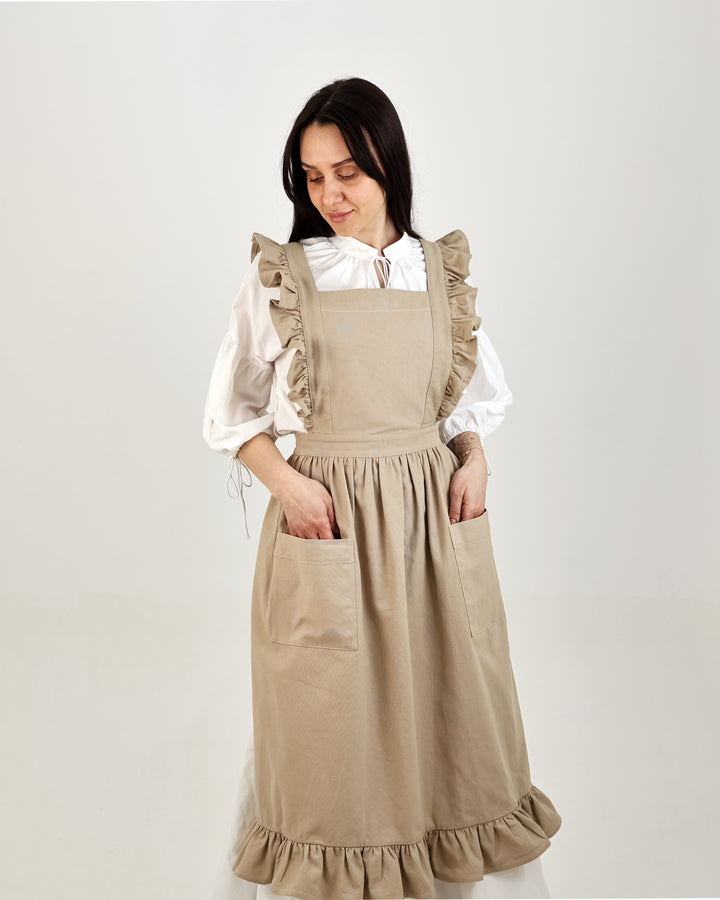 Woman wearing a beige apron over a white blouse on a plain background