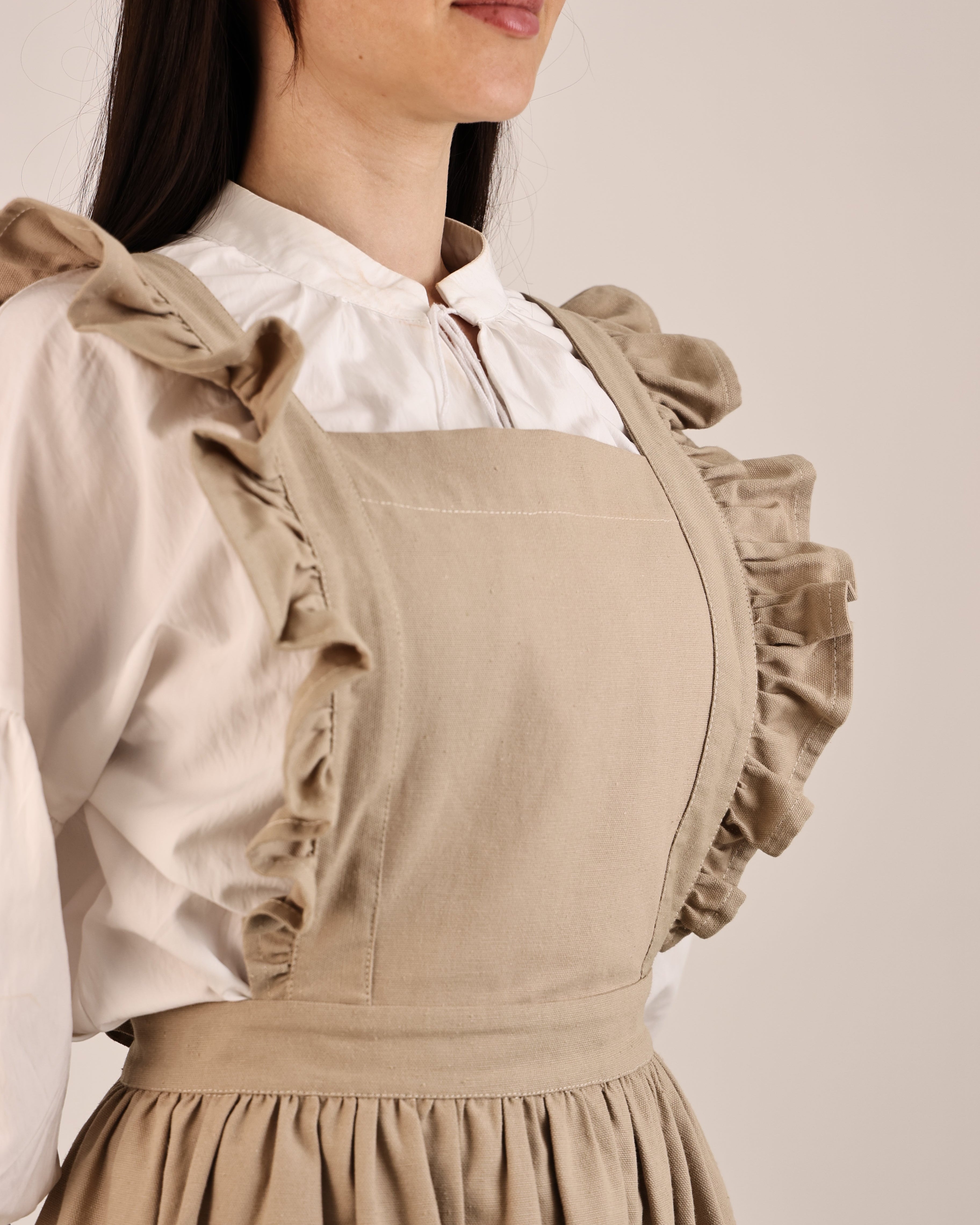 Person wearing a beige apron over a white shirt against a neutral background