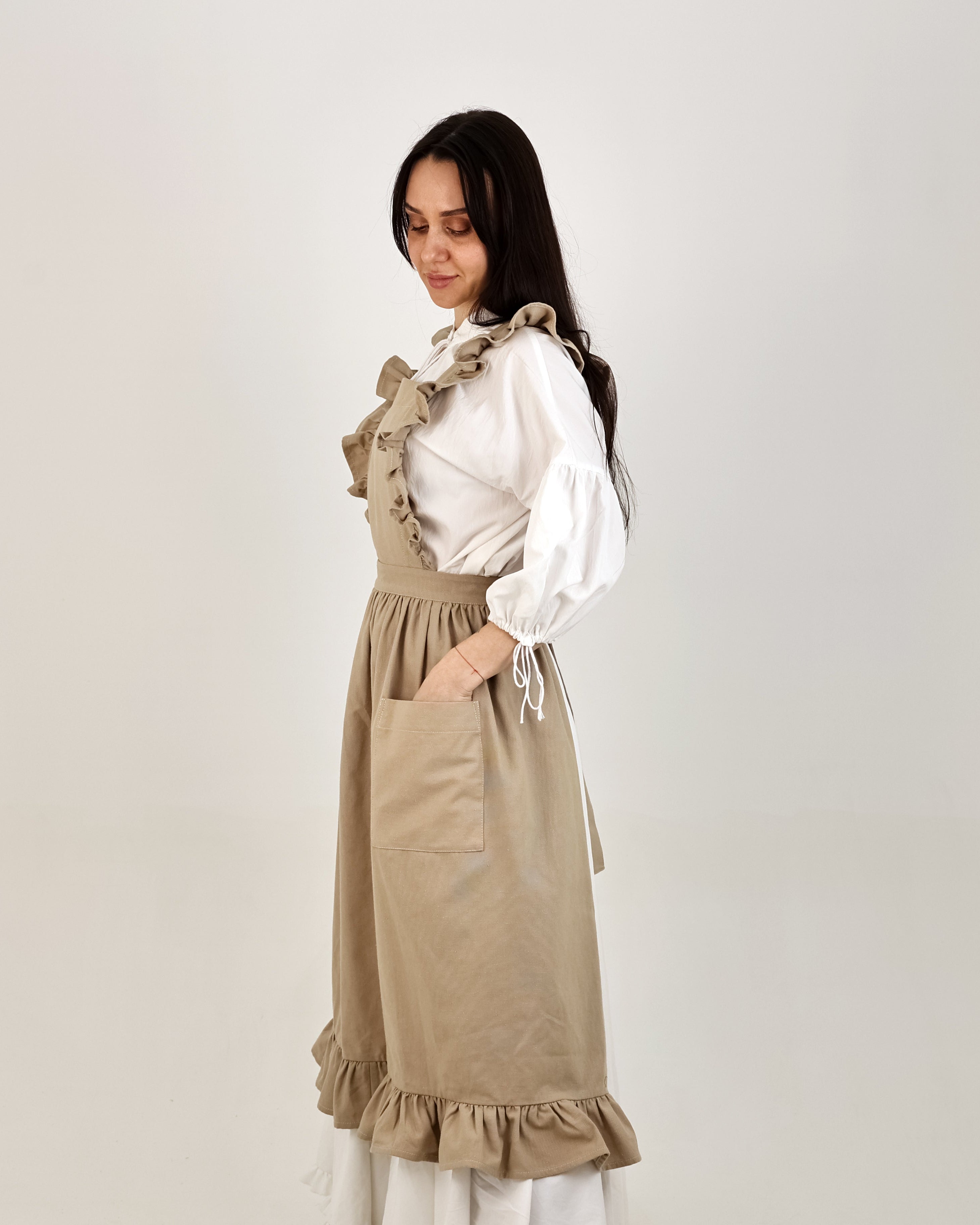 Woman wearing a beige apron over a white blouse on a plain background