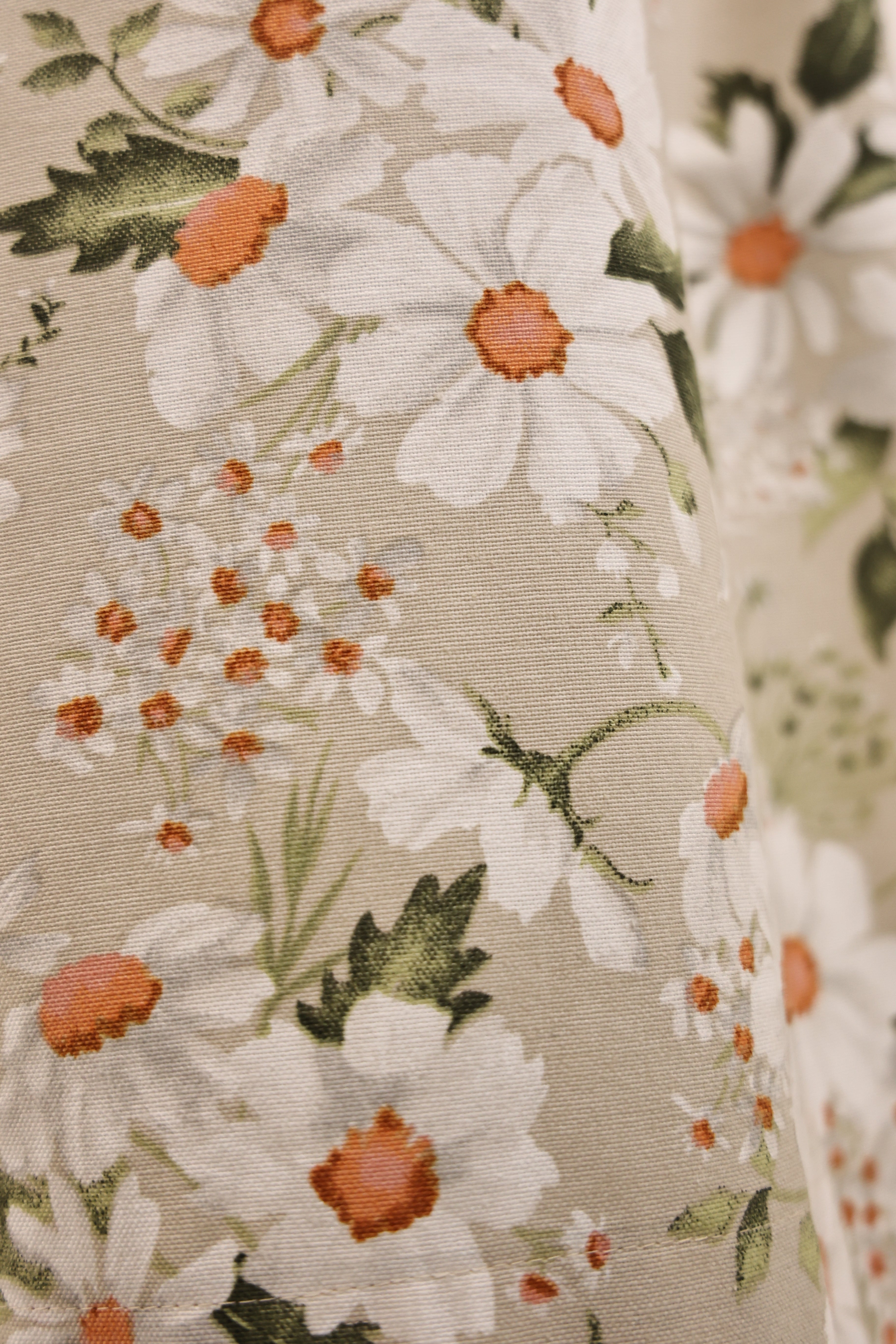 Close-up of floral fabric with white and orange flowers on a beige background