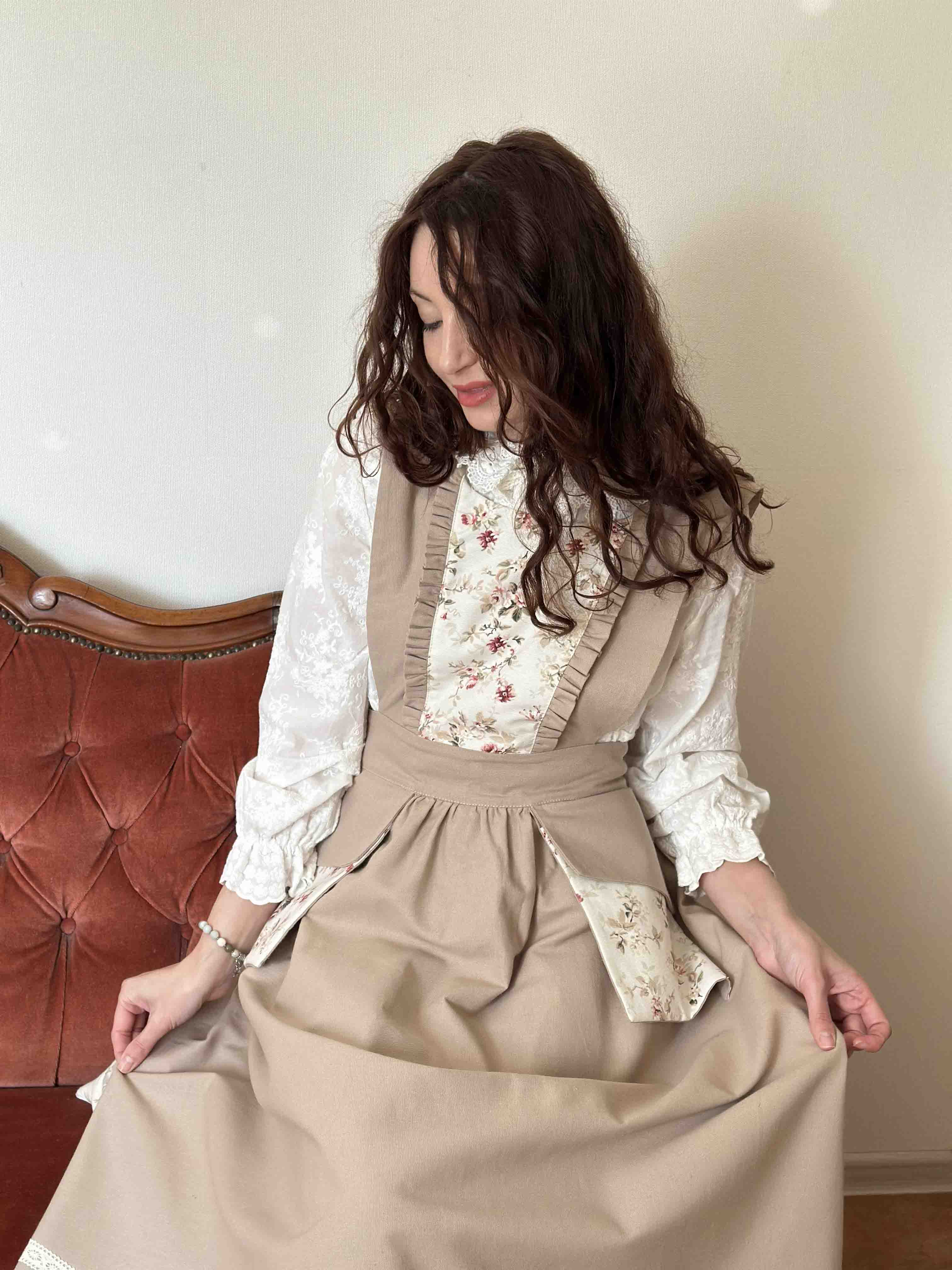 Woman wearing a vintage-style outfit with a beige apron and floral blouse against a neutral background.