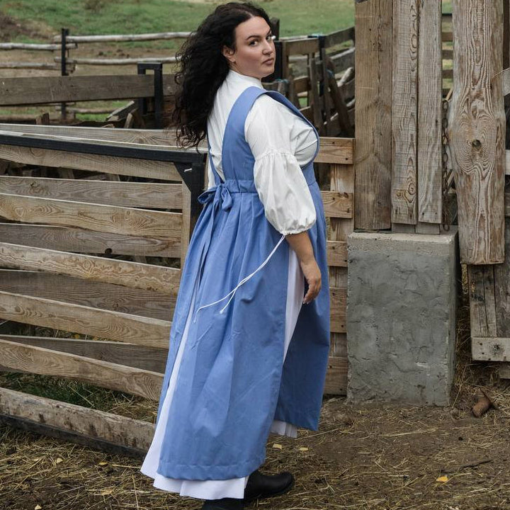 Woman in a blue dress standing in front of wooden fences on a farm.