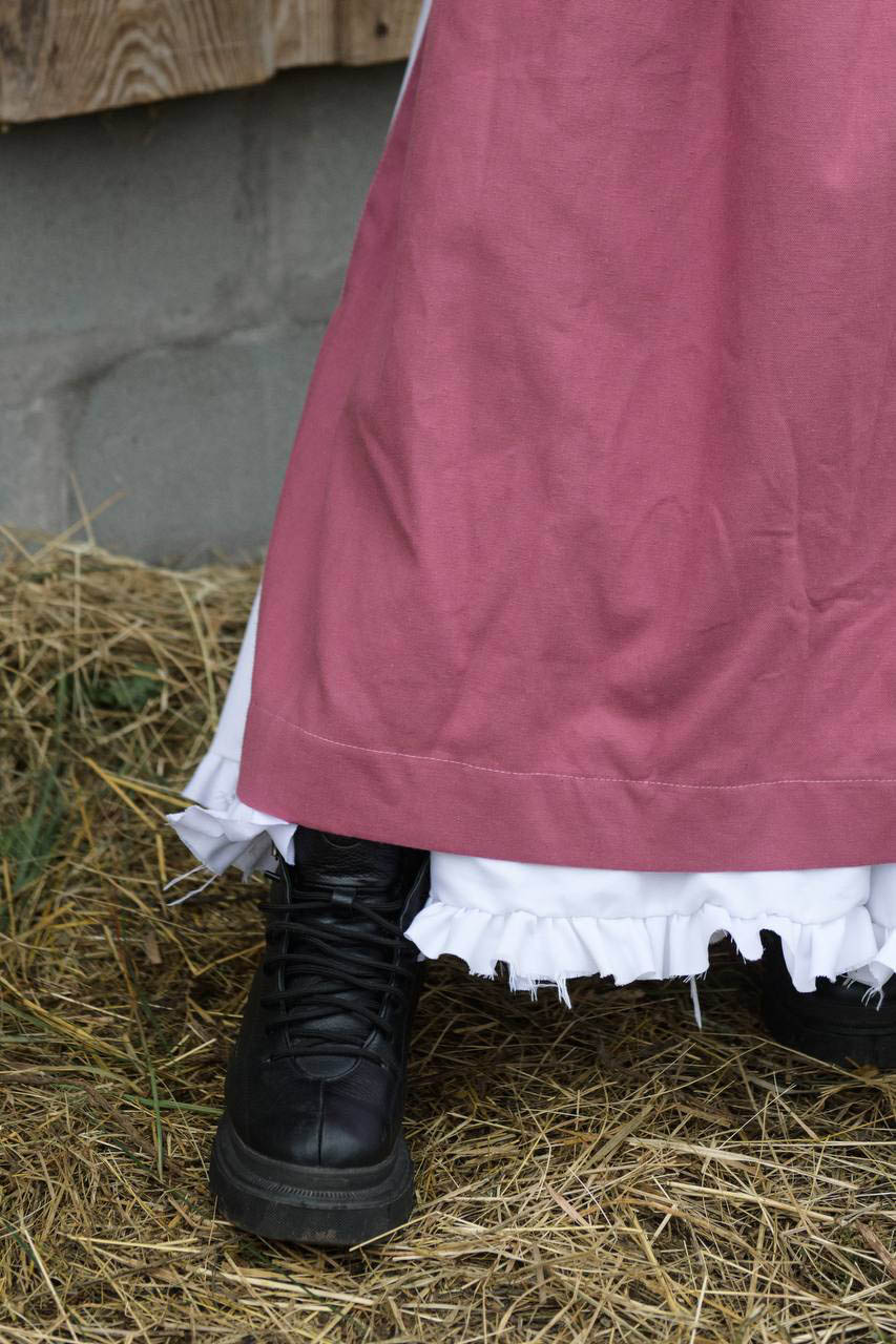 Person wearing a pink skirt and black boots on hay with a concrete wall in the background