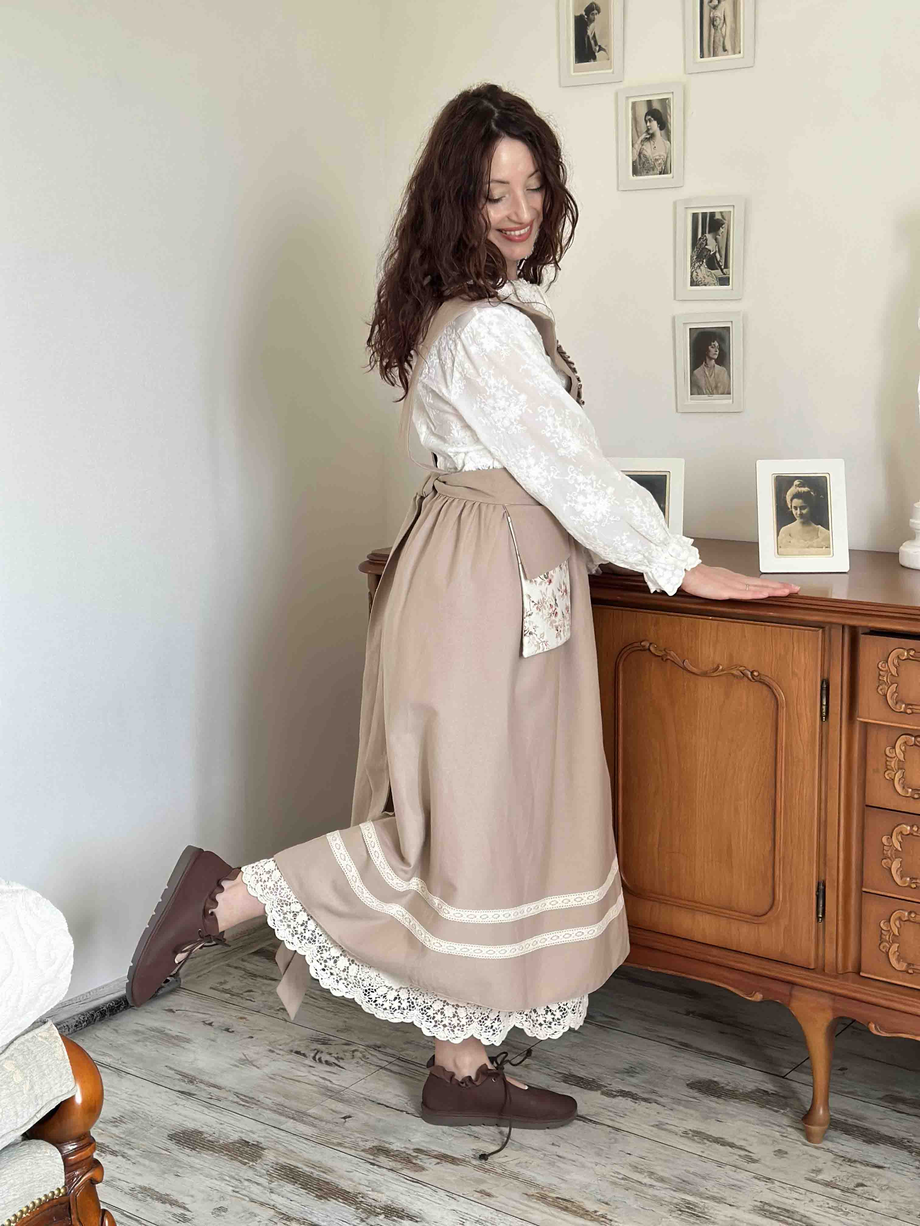 Woman in a white blouse and beige skirt standing in a room with wooden furniture and framed pictures on the wall.