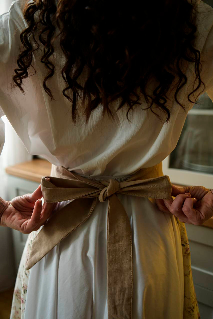 Person wearing a white blouse with a beige belt and yellow skirt, standing indoors.