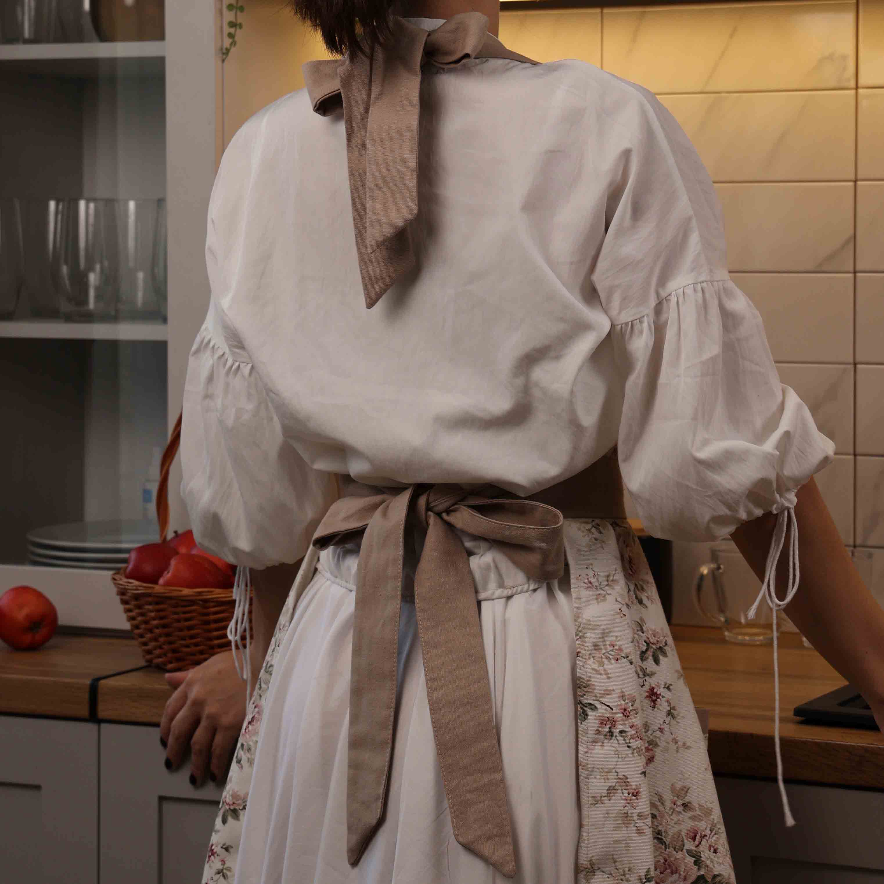 Person ironing a white shirt with large bows in a kitchen.