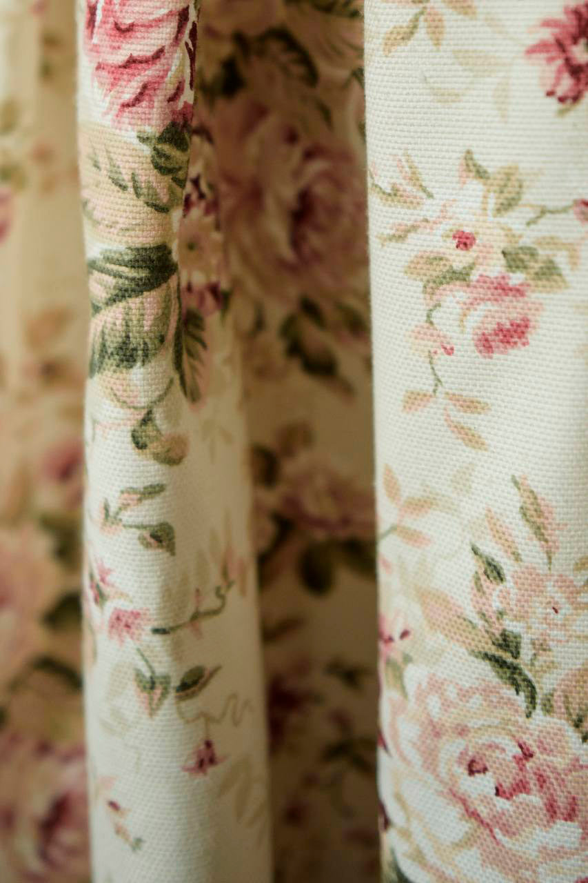 Close-up of floral fabric with pink roses and green leaves on a beige background.