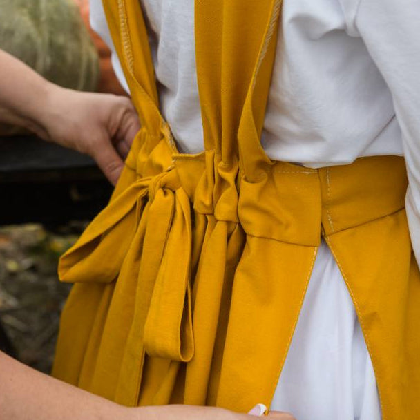 Yellow apron over a white shirt worn by a person, with a blurred background.