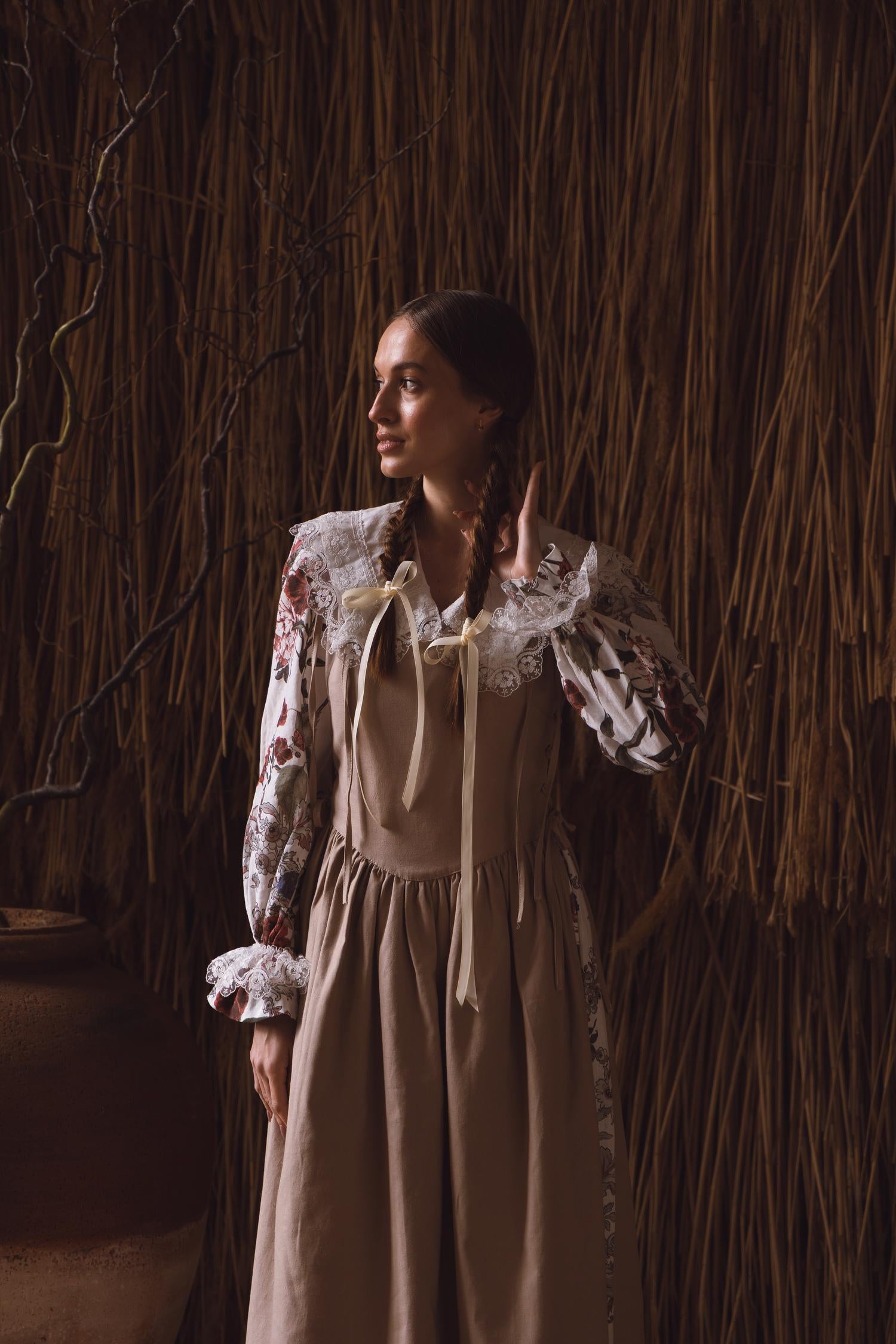 Woman in a vintage-style dress standing against a rustic wall.
