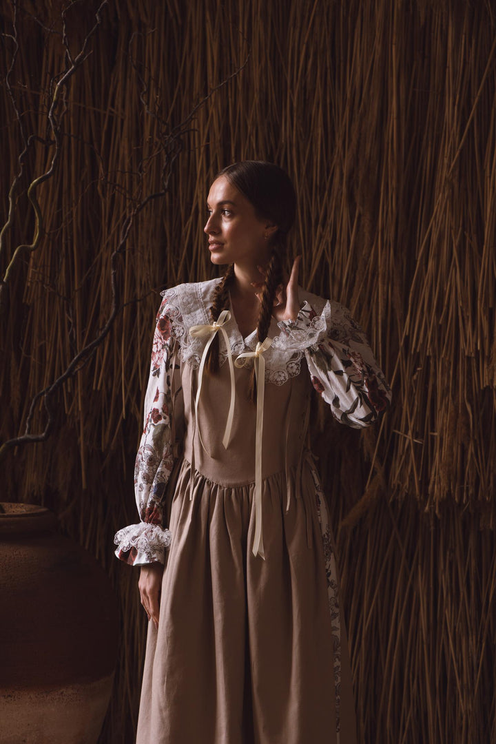 Woman in a vintage-style dress standing against a rustic wall.