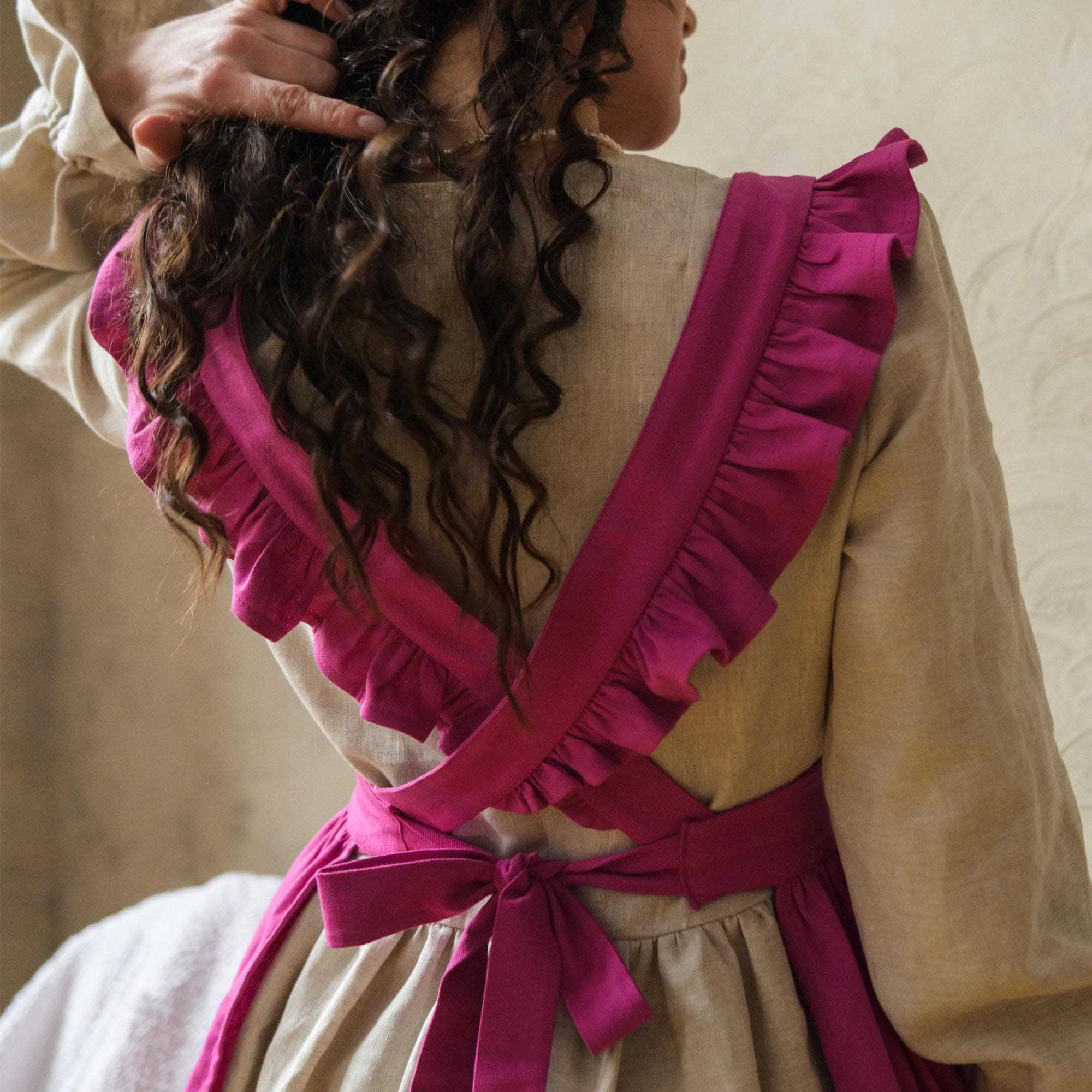 Person wearing a beige apron with a pink ruffled apron against a neutral background