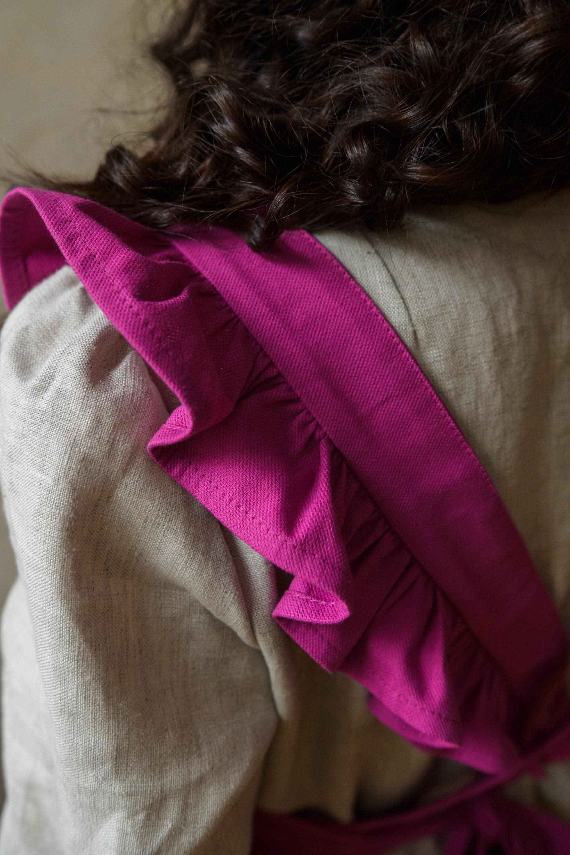 Close-up of a person wearing a pink ruffled garment over a beige sweater.