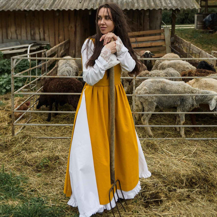 Woman in a yellow and white pinafore apron standing in a barn with sheep.