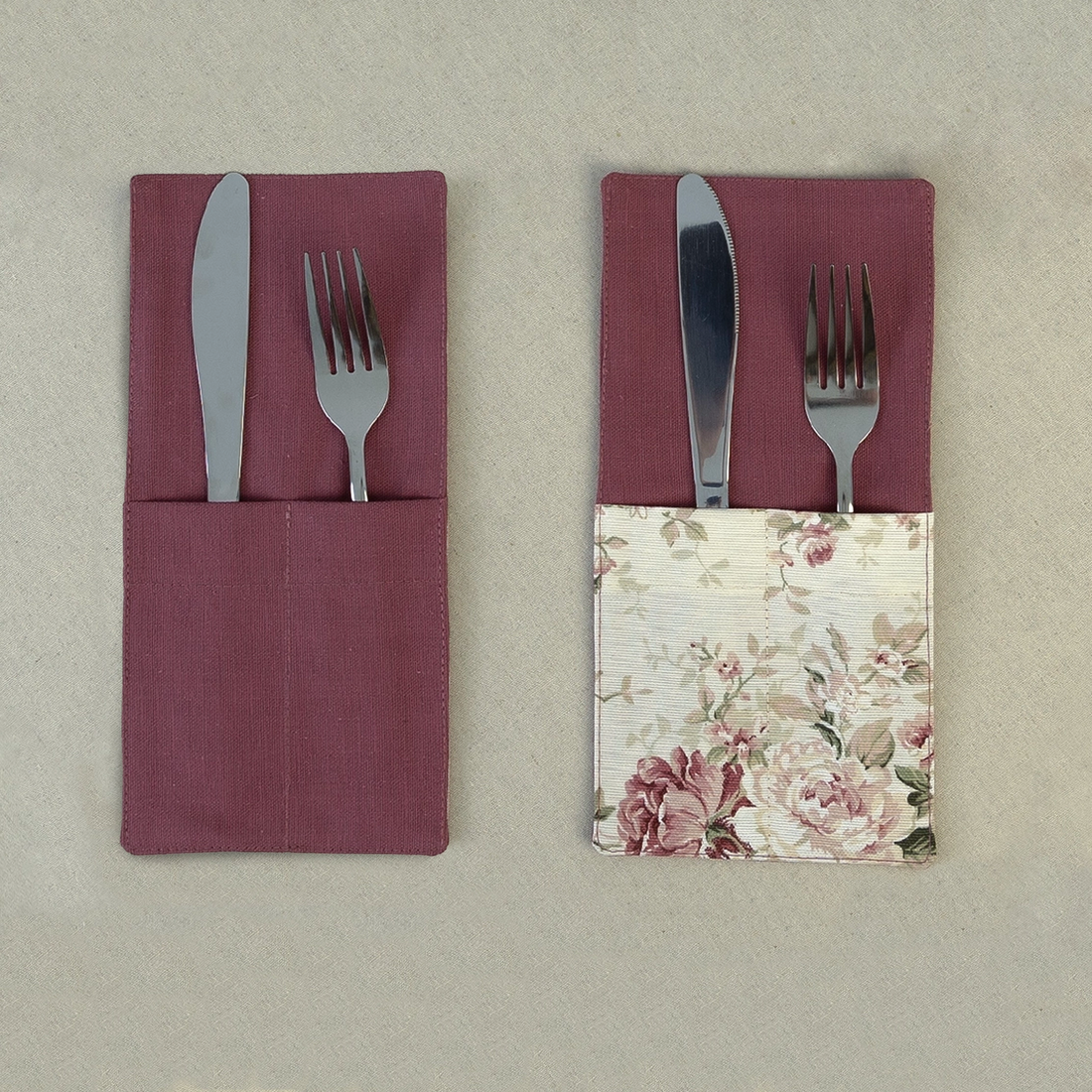 Two deep burgundy cutlery pockets holding a knife and fork, one plain and one with a rose print panel