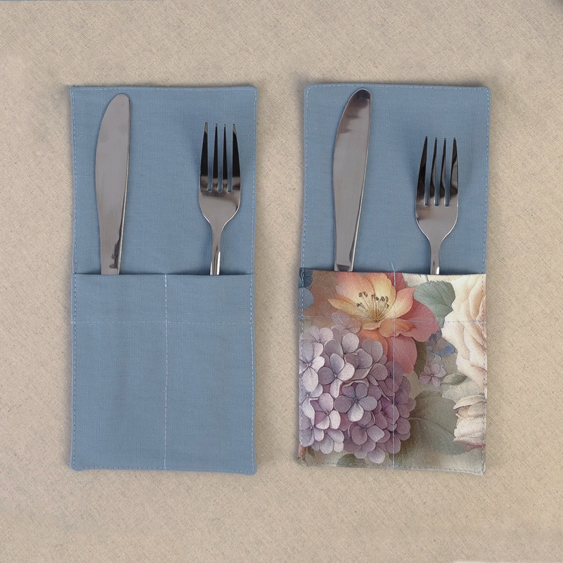 Two dusty blue cutlery pockets holding a knife and fork, one plain and one with a hydrangea print panel