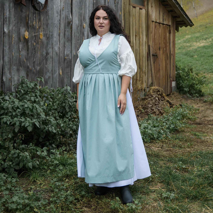Woman in a light blue dress standing in front of a wooden building.