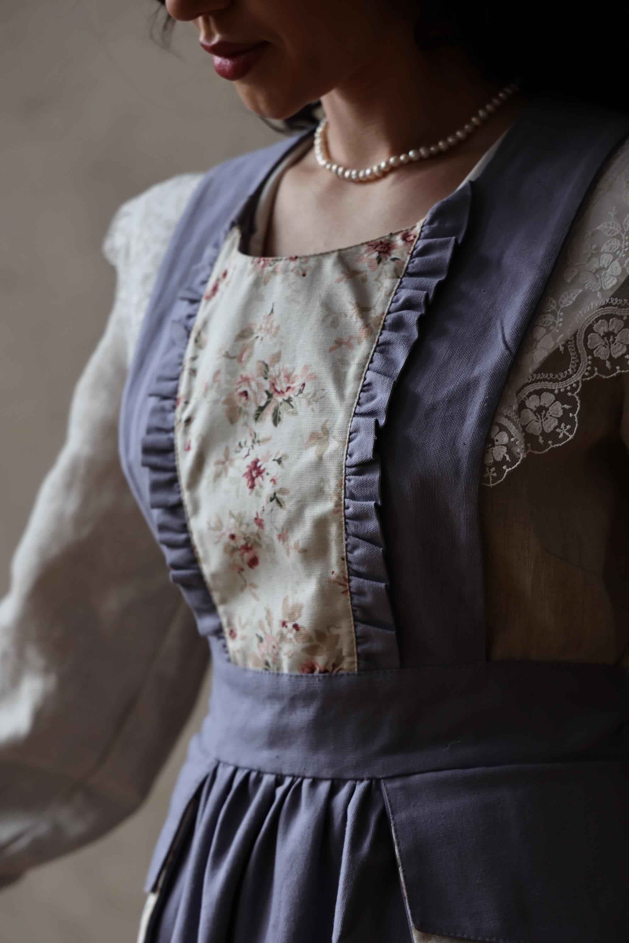 Person wearing a floral apron over a light-colored shirt with a neutral background
