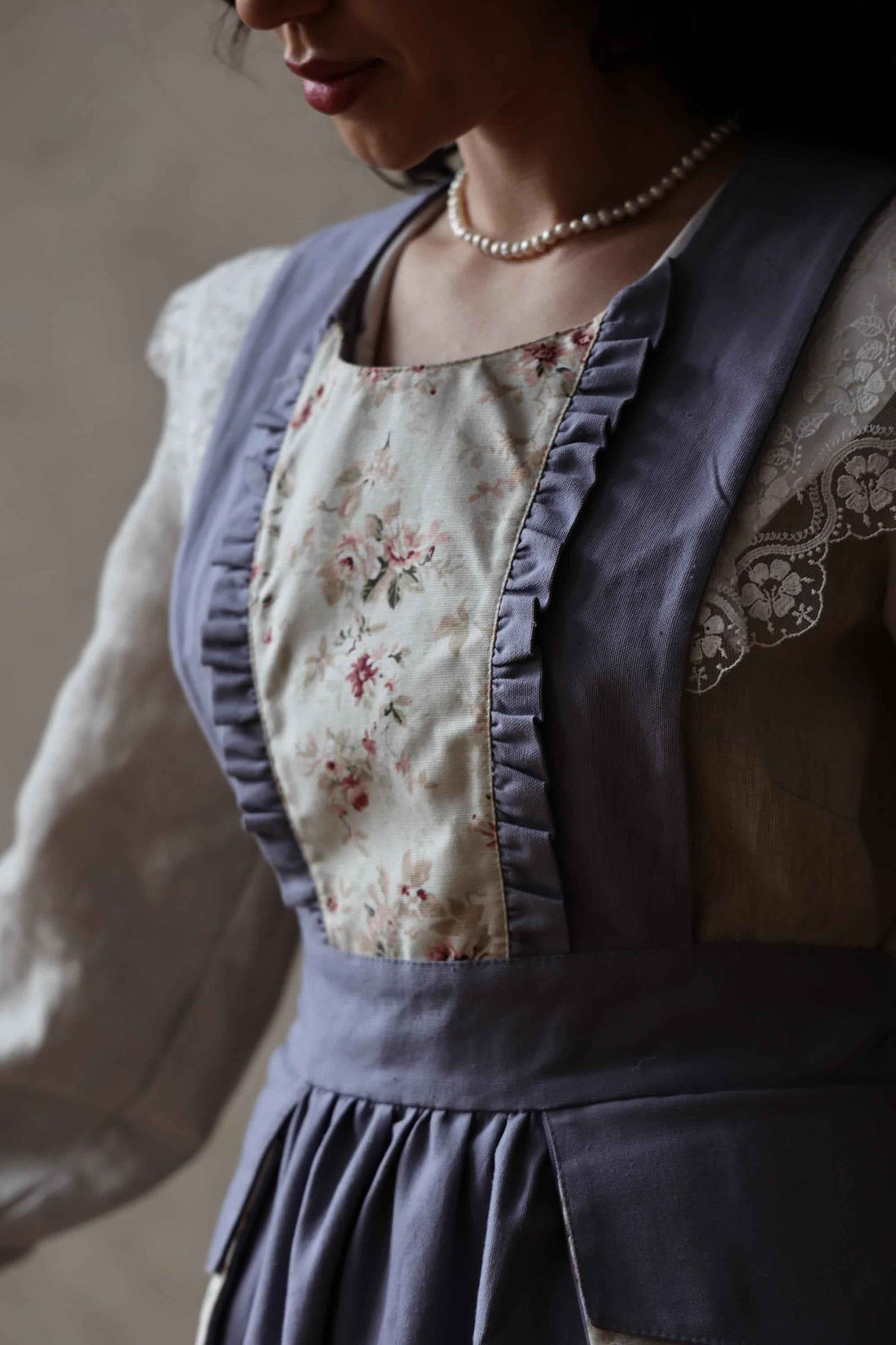 Person wearing a floral apron over a light-colored shirt with a neutral background