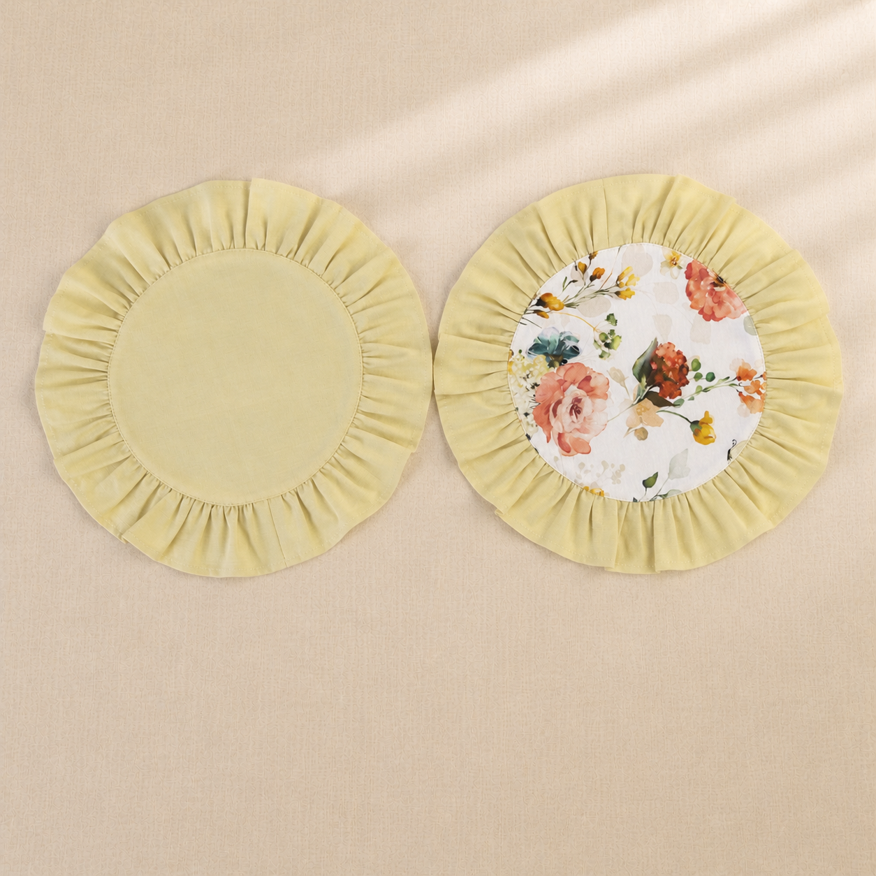 Two round butter yellow ruffle placemats, one plain and one with a peach rose print centre