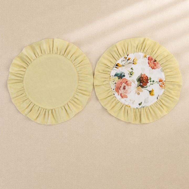 Two round butter yellow ruffle placemats, one plain and one with a peach rose print centre