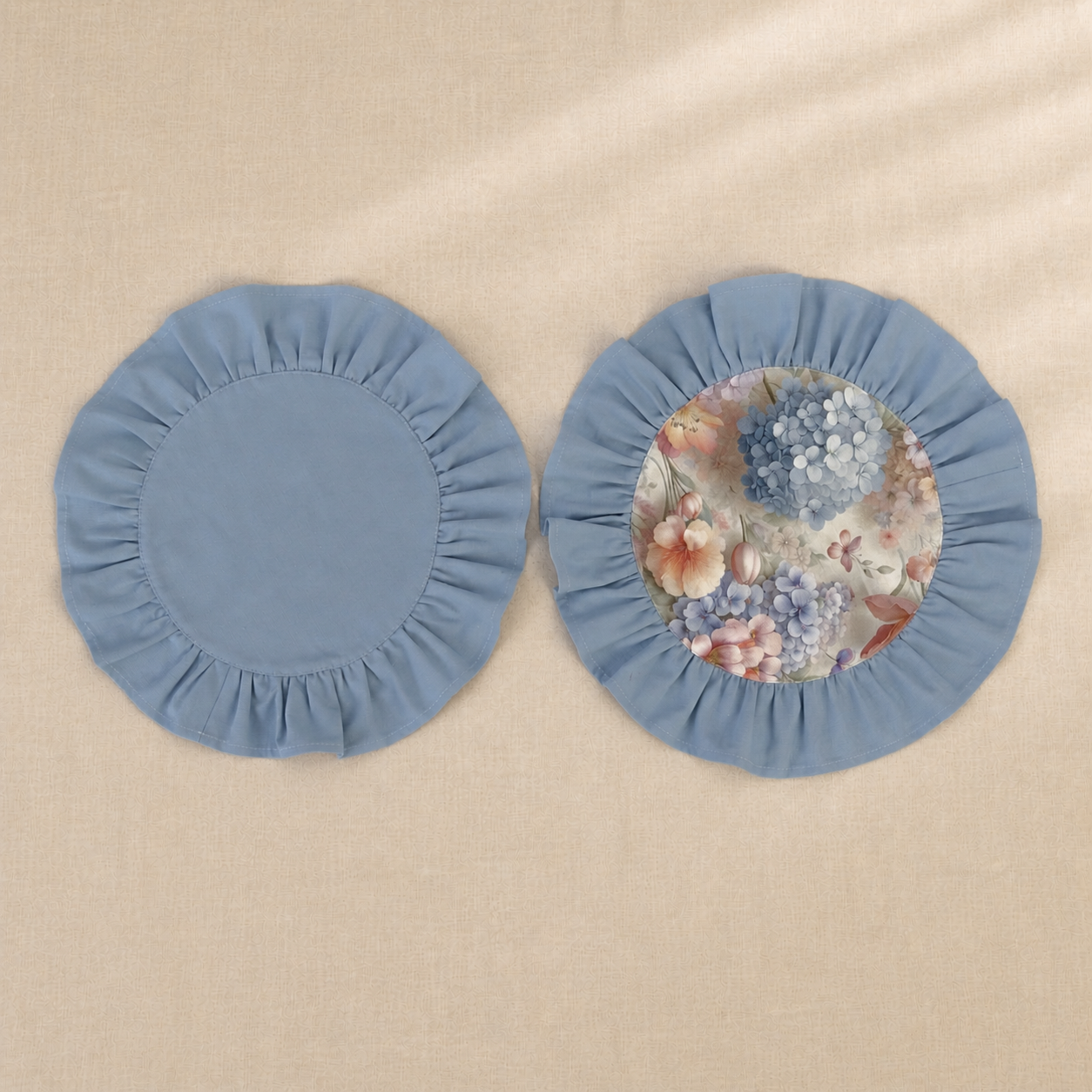 Two round dusty blue ruffle placemats, one plain and one with a hydrangea print centre