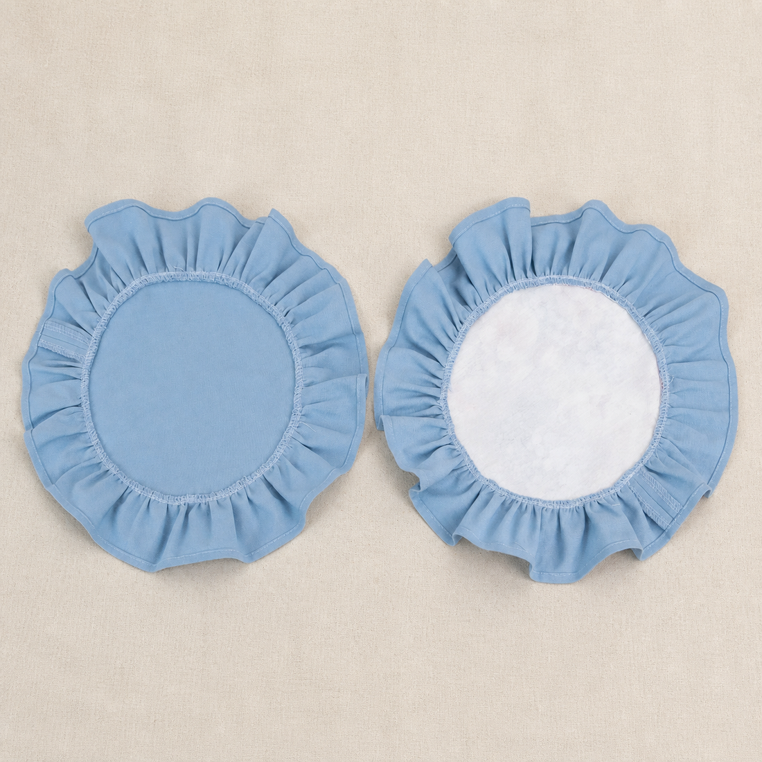 Two round dusty blue ruffle placemats, one plain and one with a white centre panel
