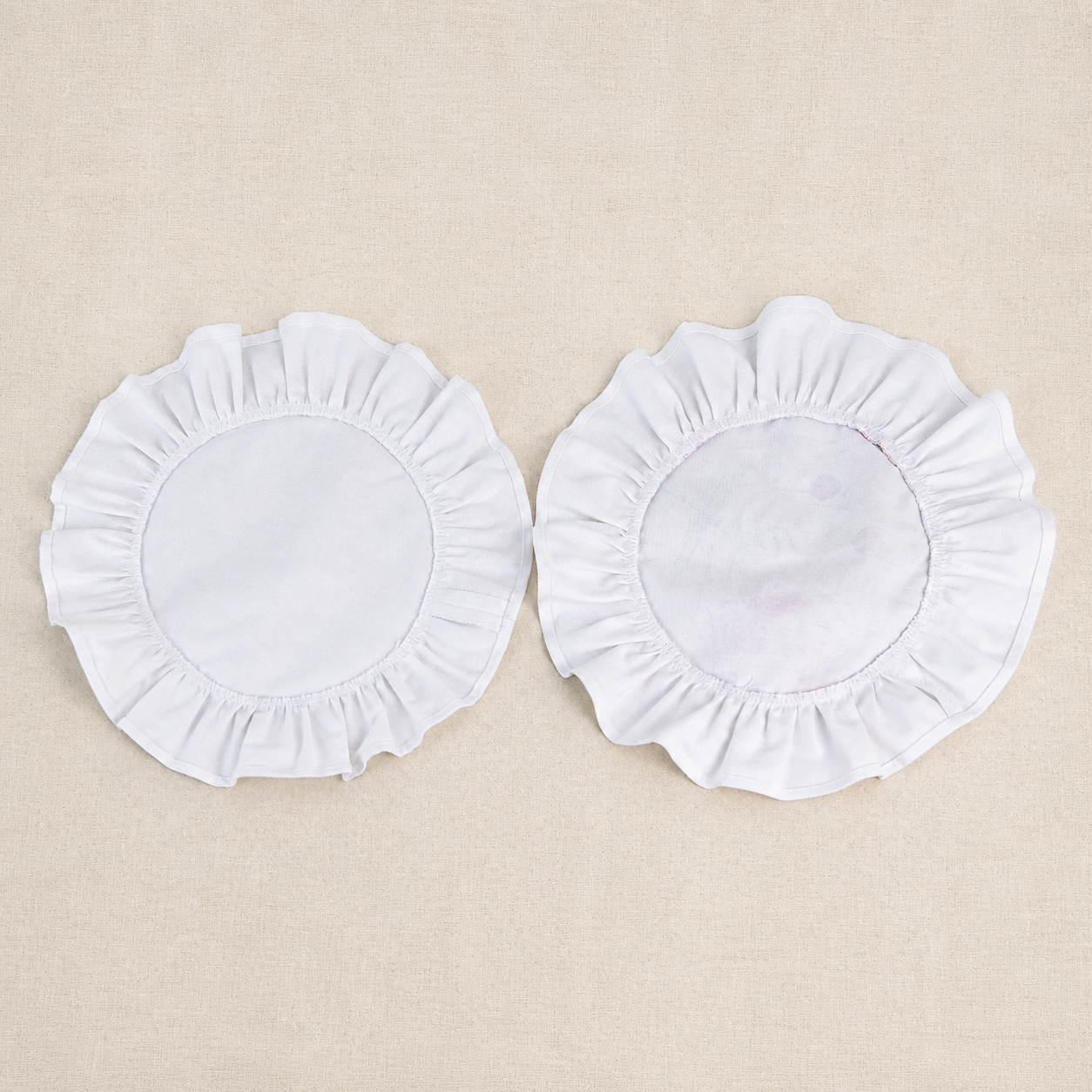 Two round soft white ruffle placemats, one plain and one with a white centre panel