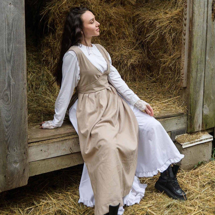 Woman in historical attire sitting on a wooden bench with hay in the background