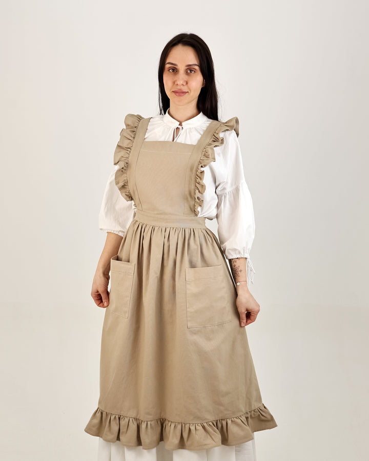 Woman wearing a beige apron over a white blouse on a plain background