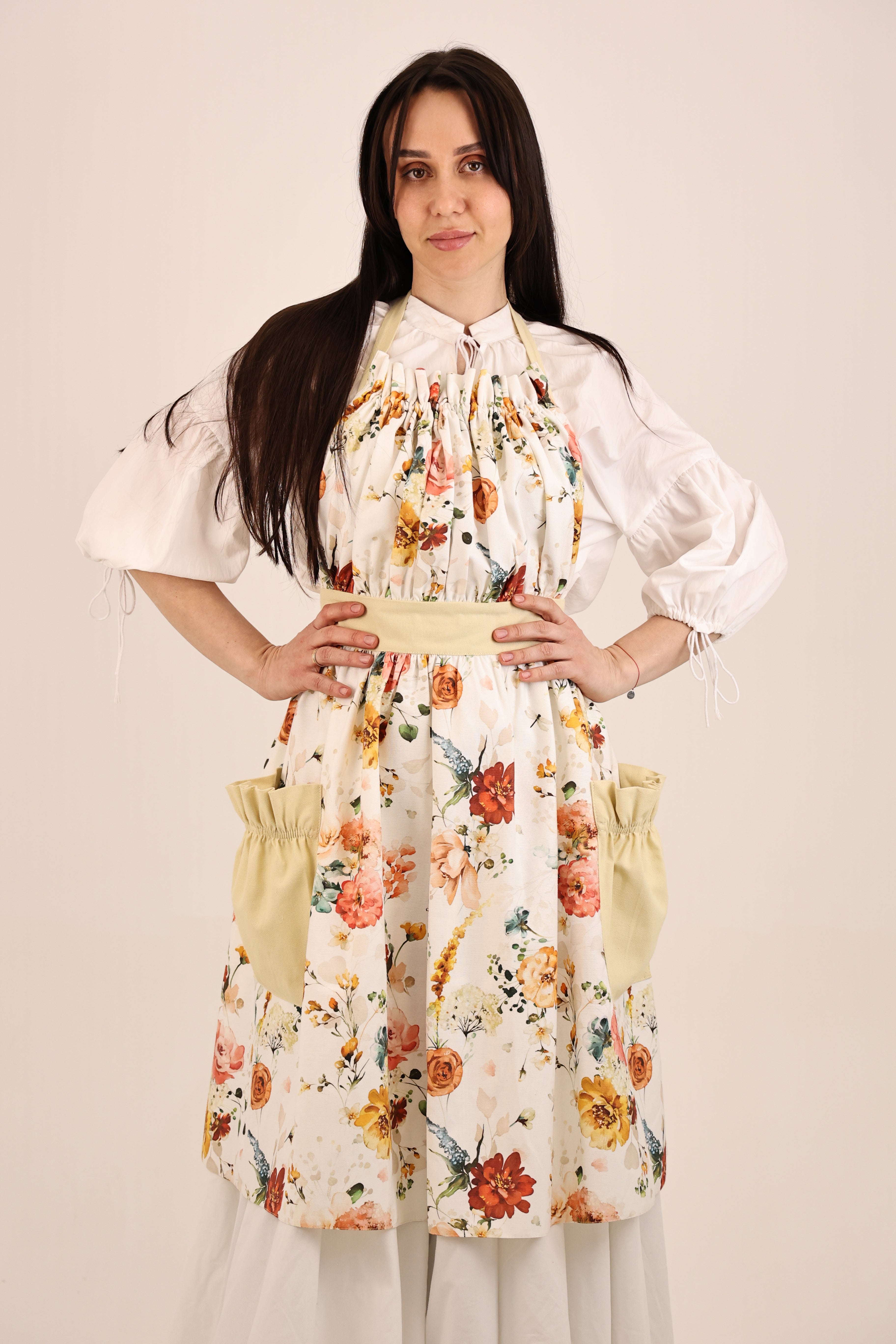 Woman wearing a floral dress with puffed sleeves and apron on a plain background