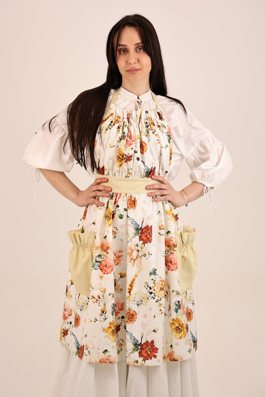 Woman wearing a floral dress with puffed sleeves and apron on a plain background